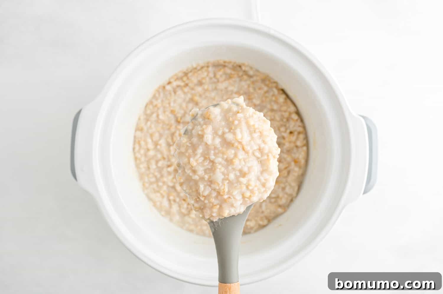 A serving spoon laden with creamy, cooked oatmeal, ready to be dished out into a bowl.
