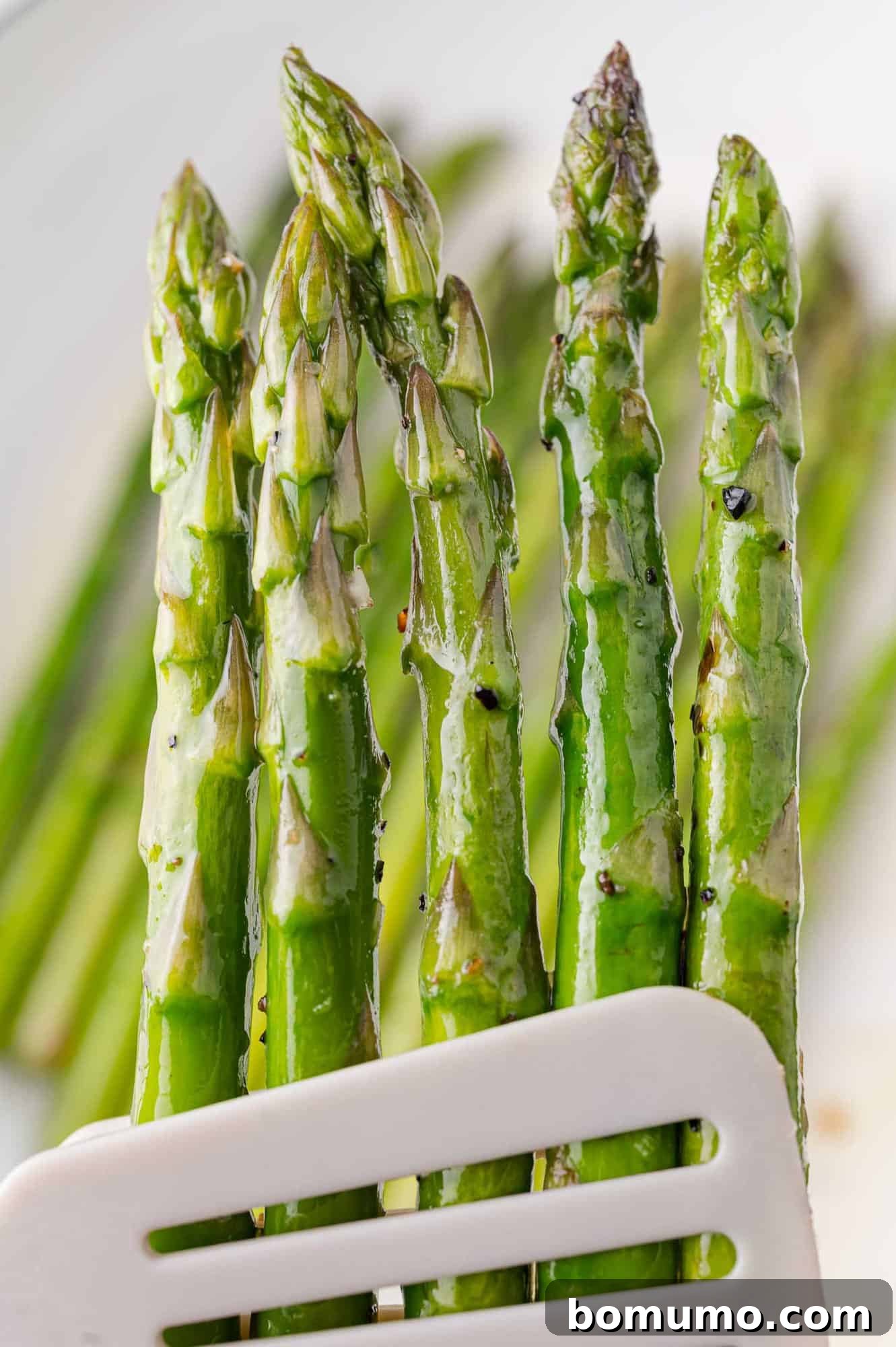 Close-up of vibrant green, crisp sautéed asparagus held with kitchen tongs.
