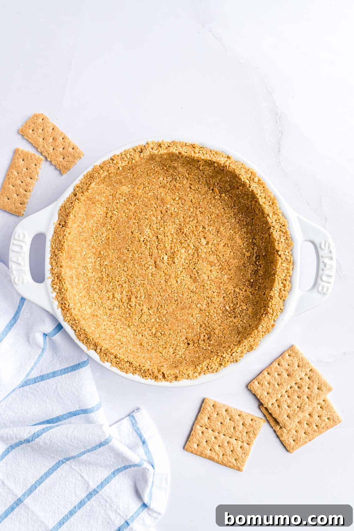 A golden brown homemade graham cracker crust neatly pressed into a classic white ceramic pie plate, ready for filling.
