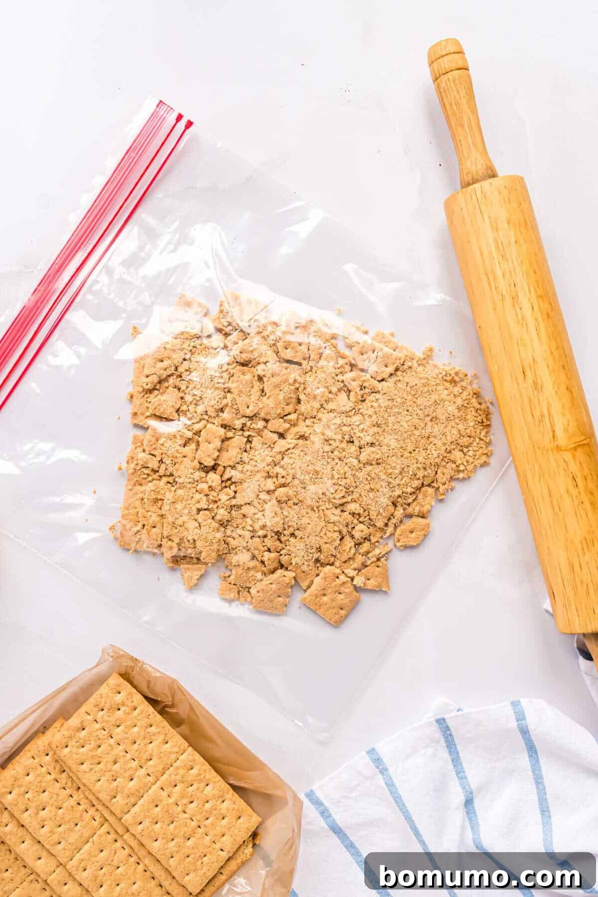 Graham crackers being crushed in a large zip-top bag using a wooden rolling pin on a wooden surface.