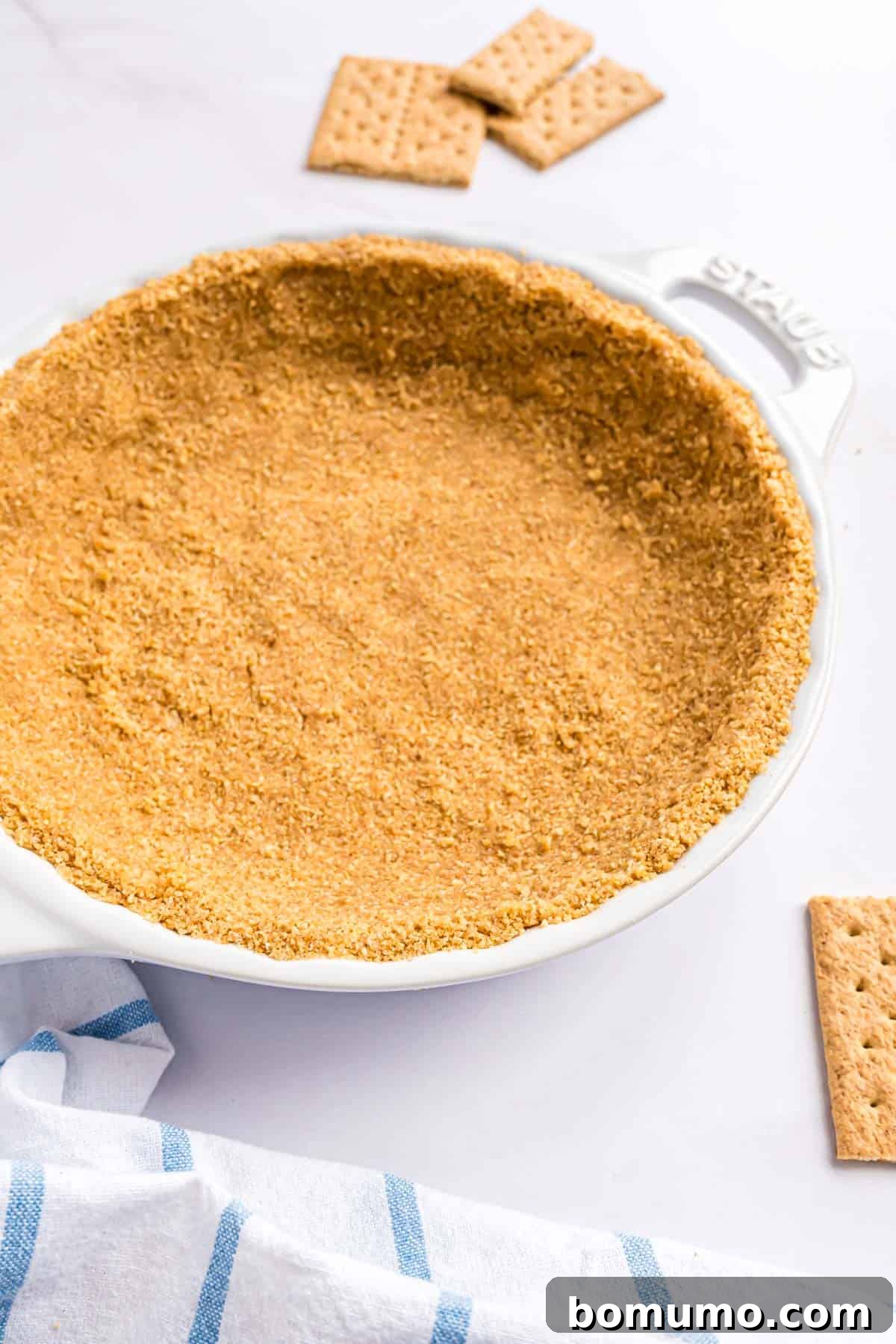 A beautifully golden homemade graham cracker crust resting in a white ceramic pie plate, showcasing its perfect texture and color.