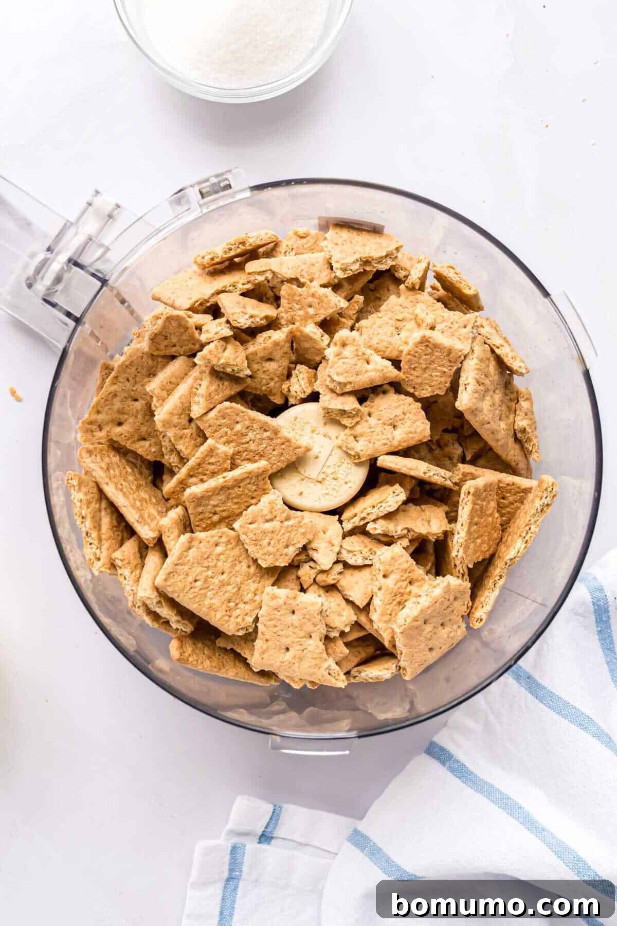 Large pieces of graham crackers placed inside a food processor bowl, ready to be crushed.