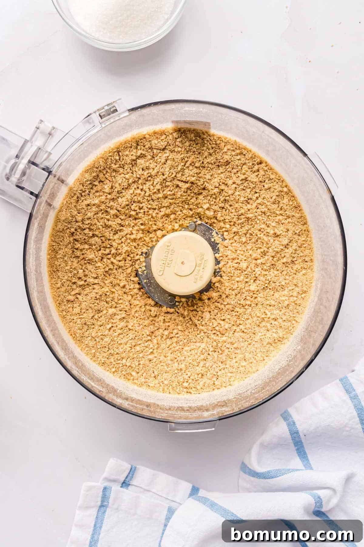 Finely crushed graham cracker crumbs filling the bottom of a food processor bowl.