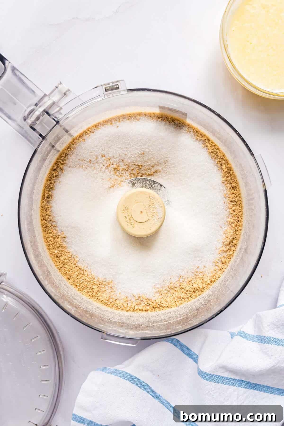 Granulated sugar freshly added to the graham cracker crumbs in a food processor.