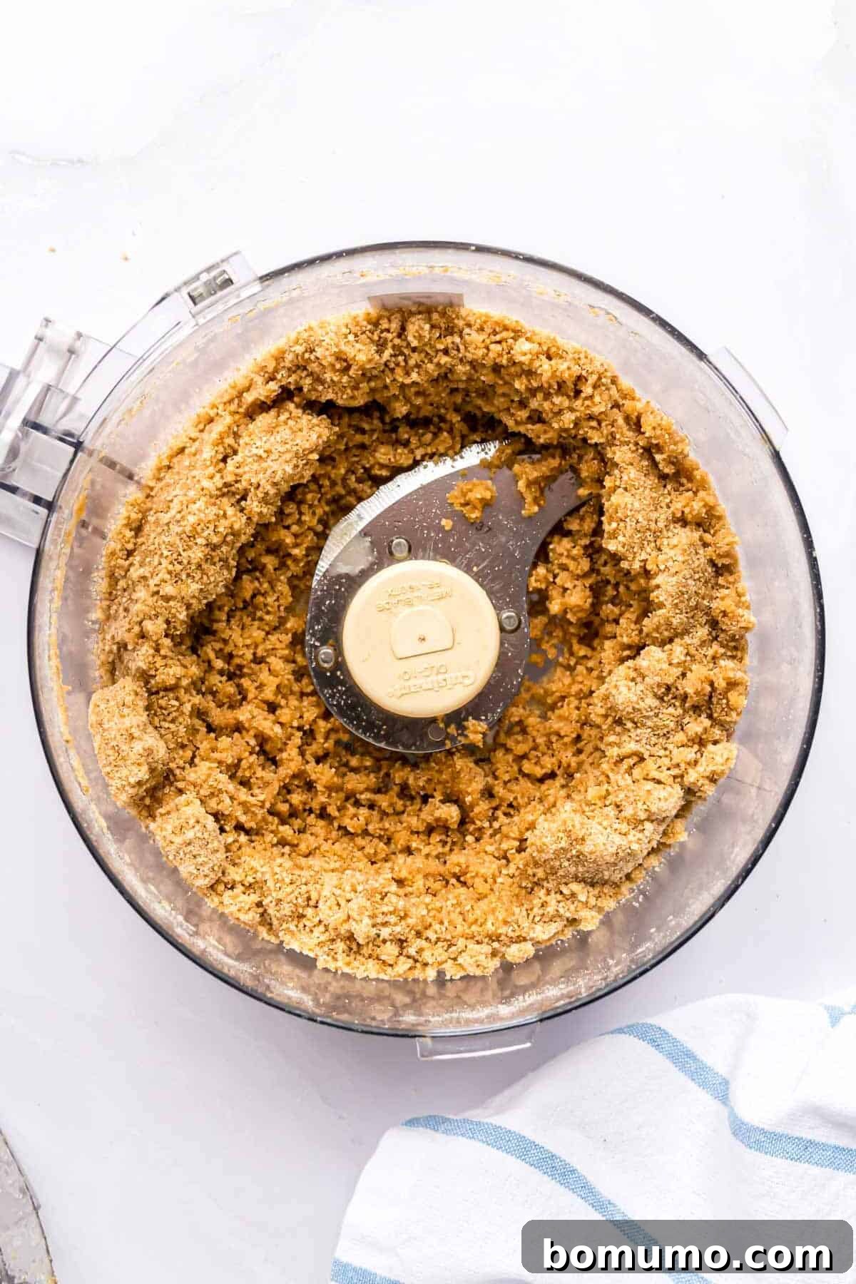 The blended graham cracker, sugar, and butter mixture, now a medium brown, resting in the food processor bowl.