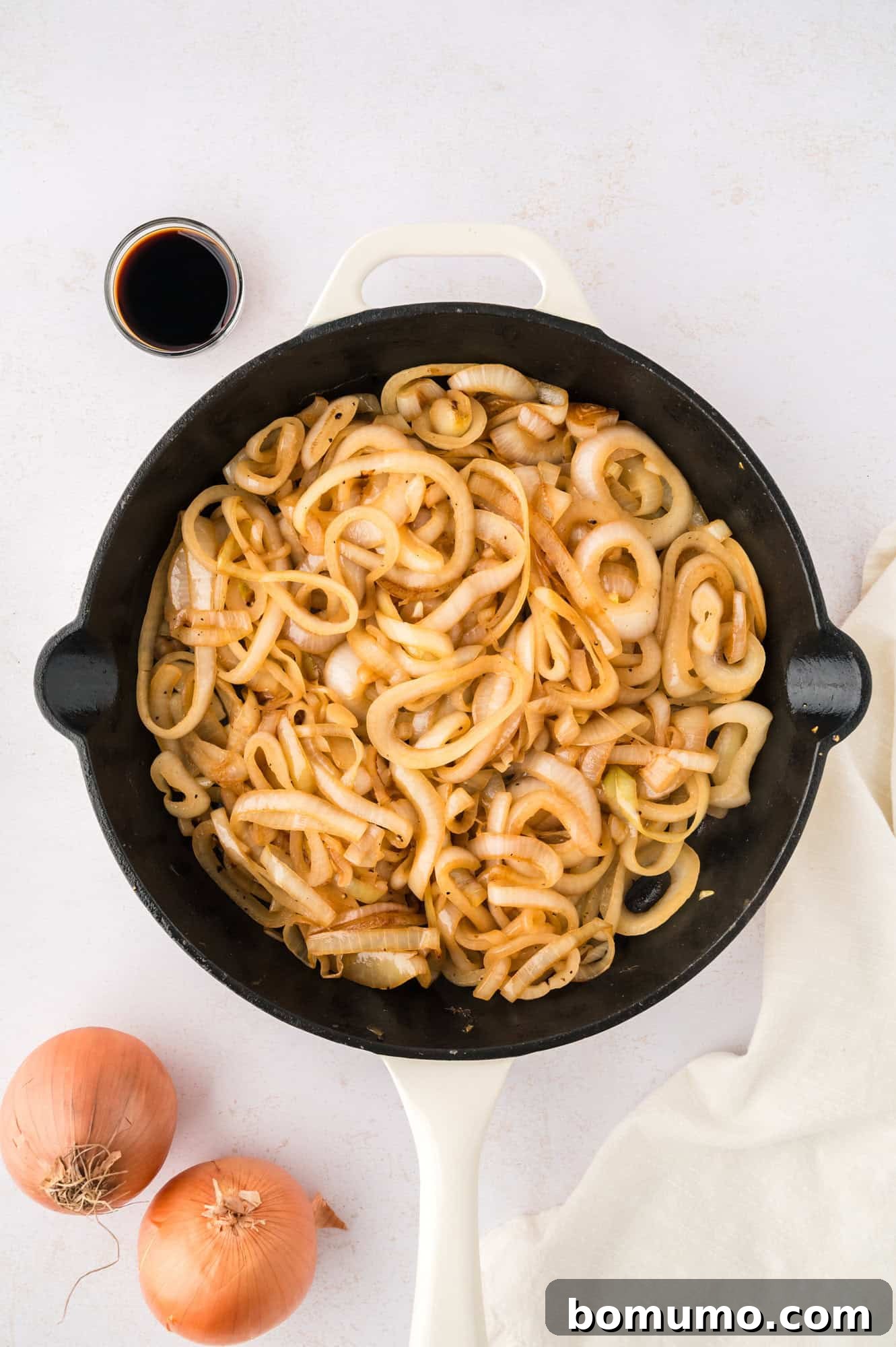 Perfectly sautéed onions, golden and tender, occupying a large black skillet with a white handle, indicating completion.