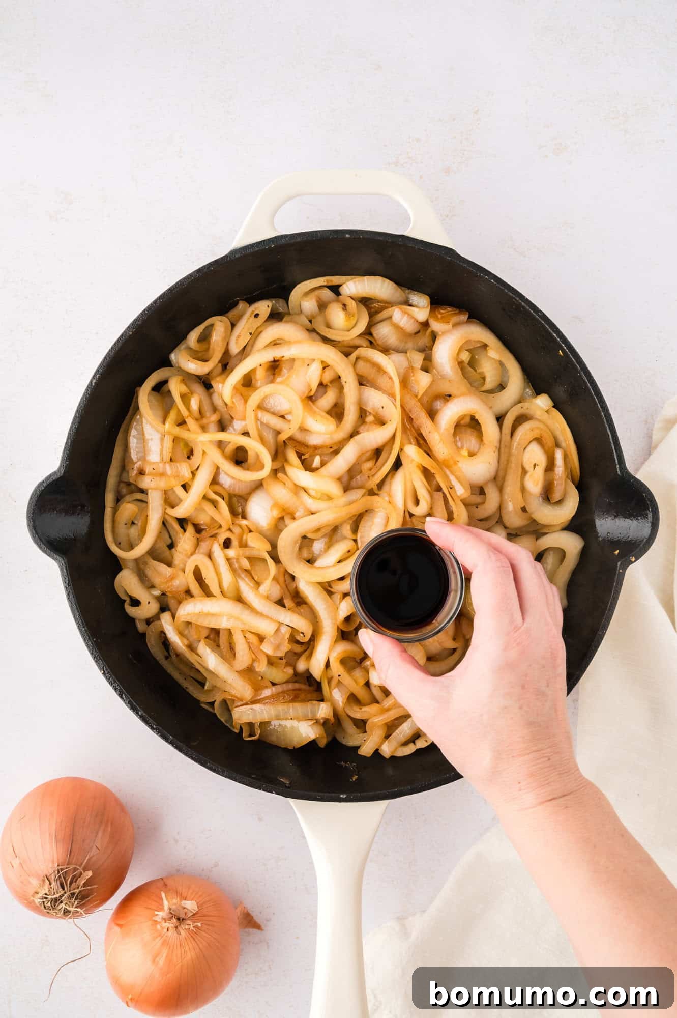 A stream of balsamic vinegar being poured over a pan of freshly sautéed onions, adding a final touch of flavor and sheen.