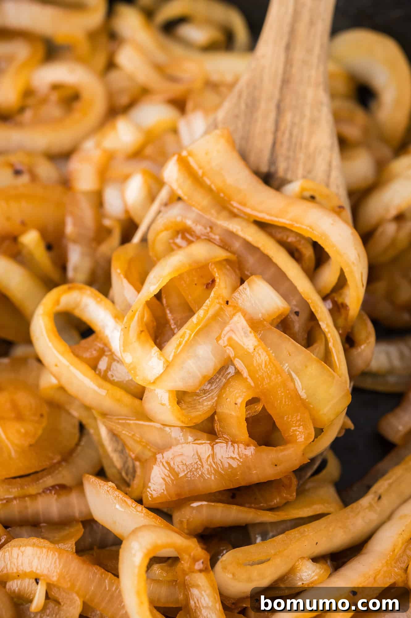 Close-up of perfectly golden and tender sautéed onions resting on a wooden spoon, highlighting their beautiful texture and readiness to be served.