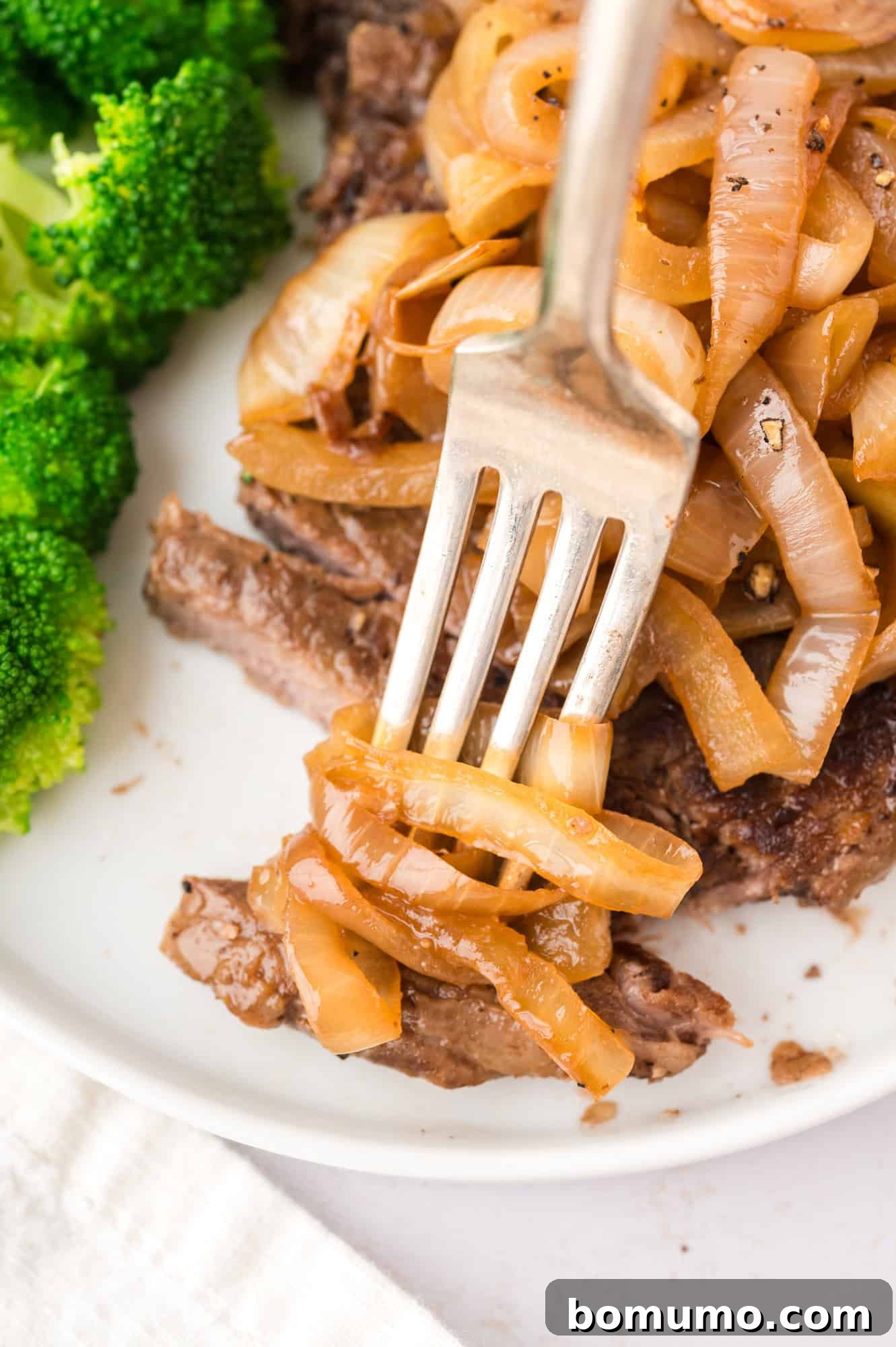 Juicy steak topped with a generous serving of golden sautéed onions and a side of fresh broccoli on a white plate, showcasing a complete and flavorful meal.