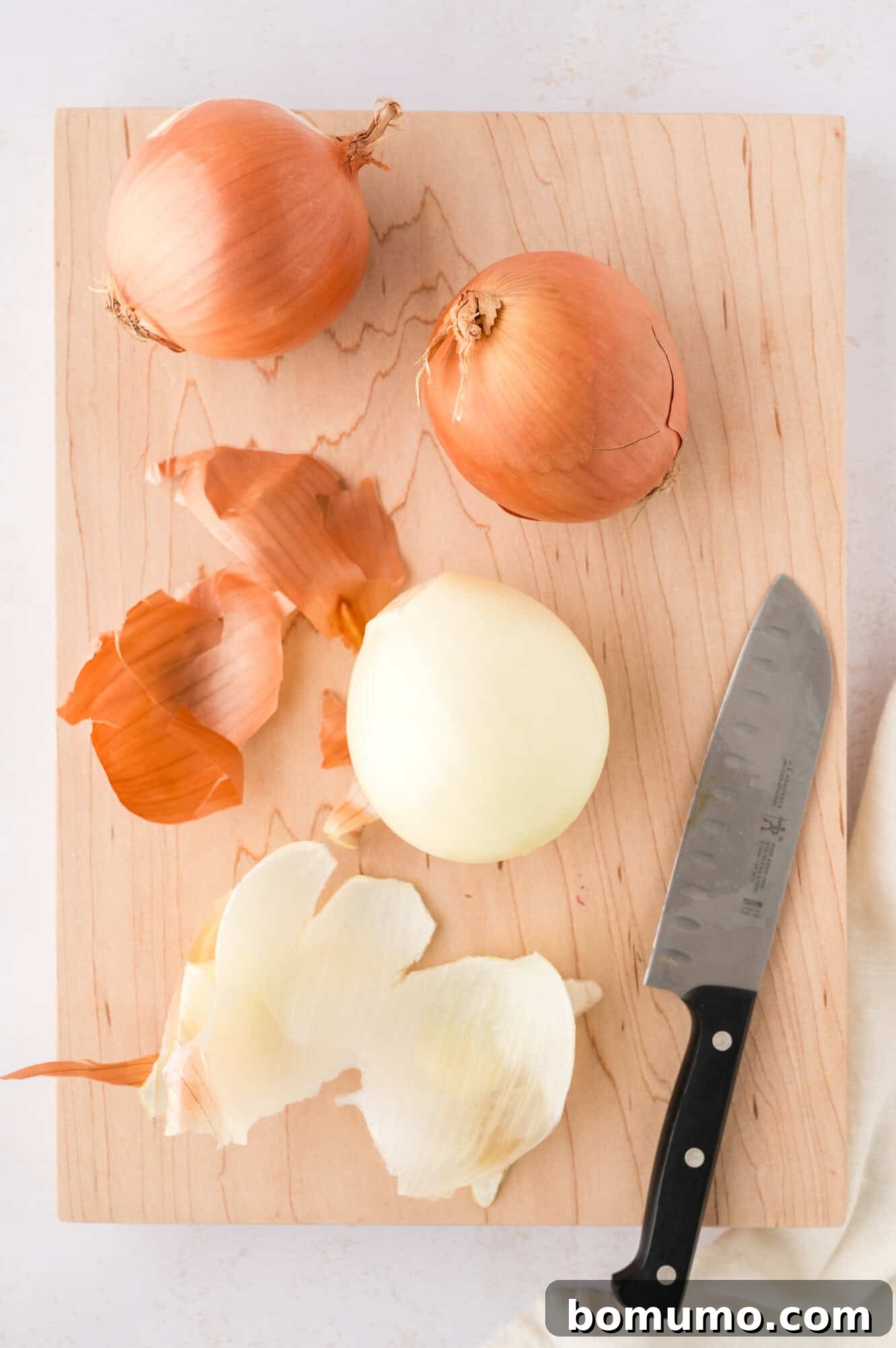 A pristine, peeled onion resting on a wooden cutting board, perfectly prepped and awaiting slicing for sautéed onions.
