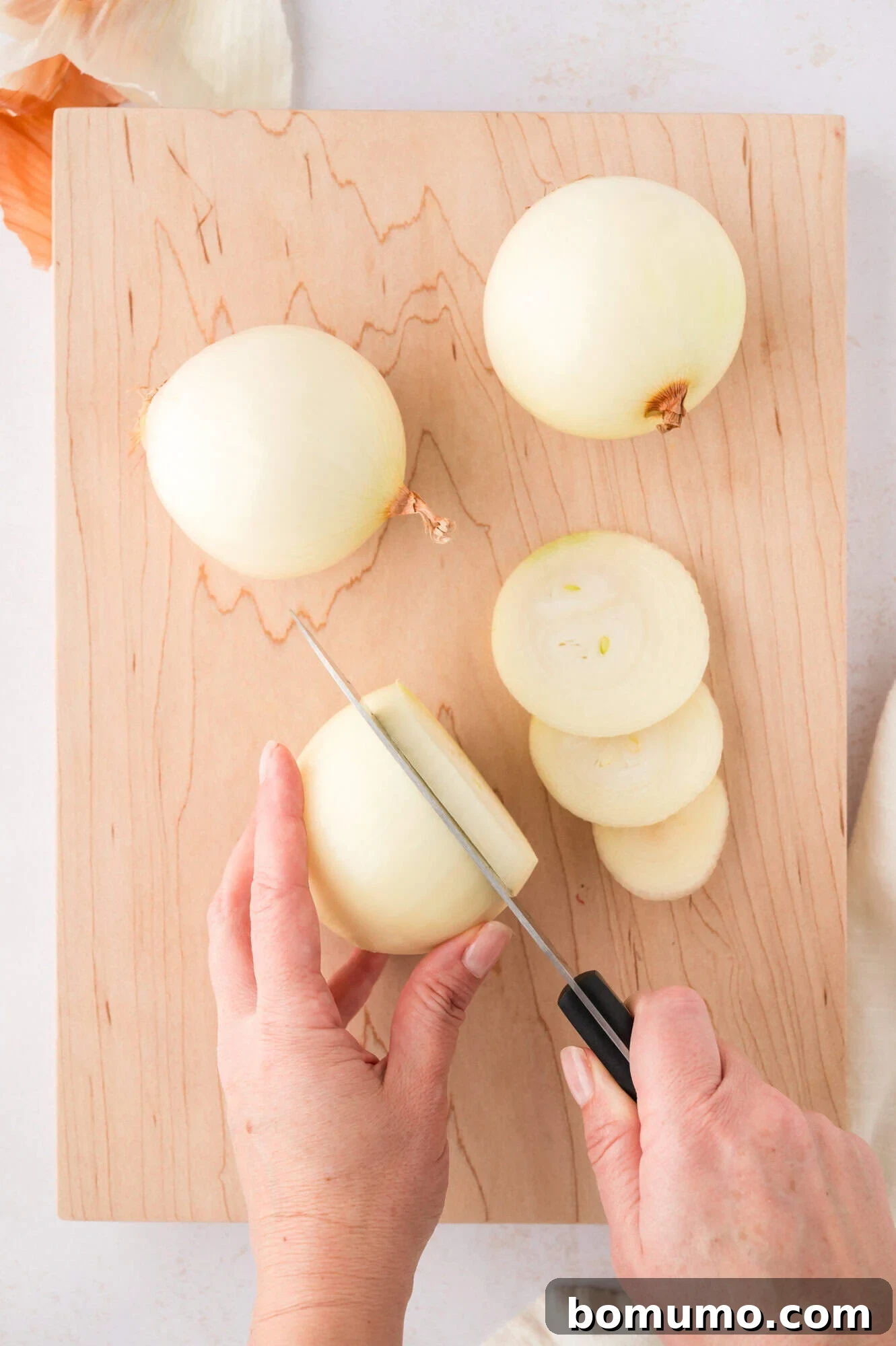 A sharp kitchen knife meticulously slicing an onion on a wooden cutting board, illustrating the precision needed for even sautéed onion pieces.
