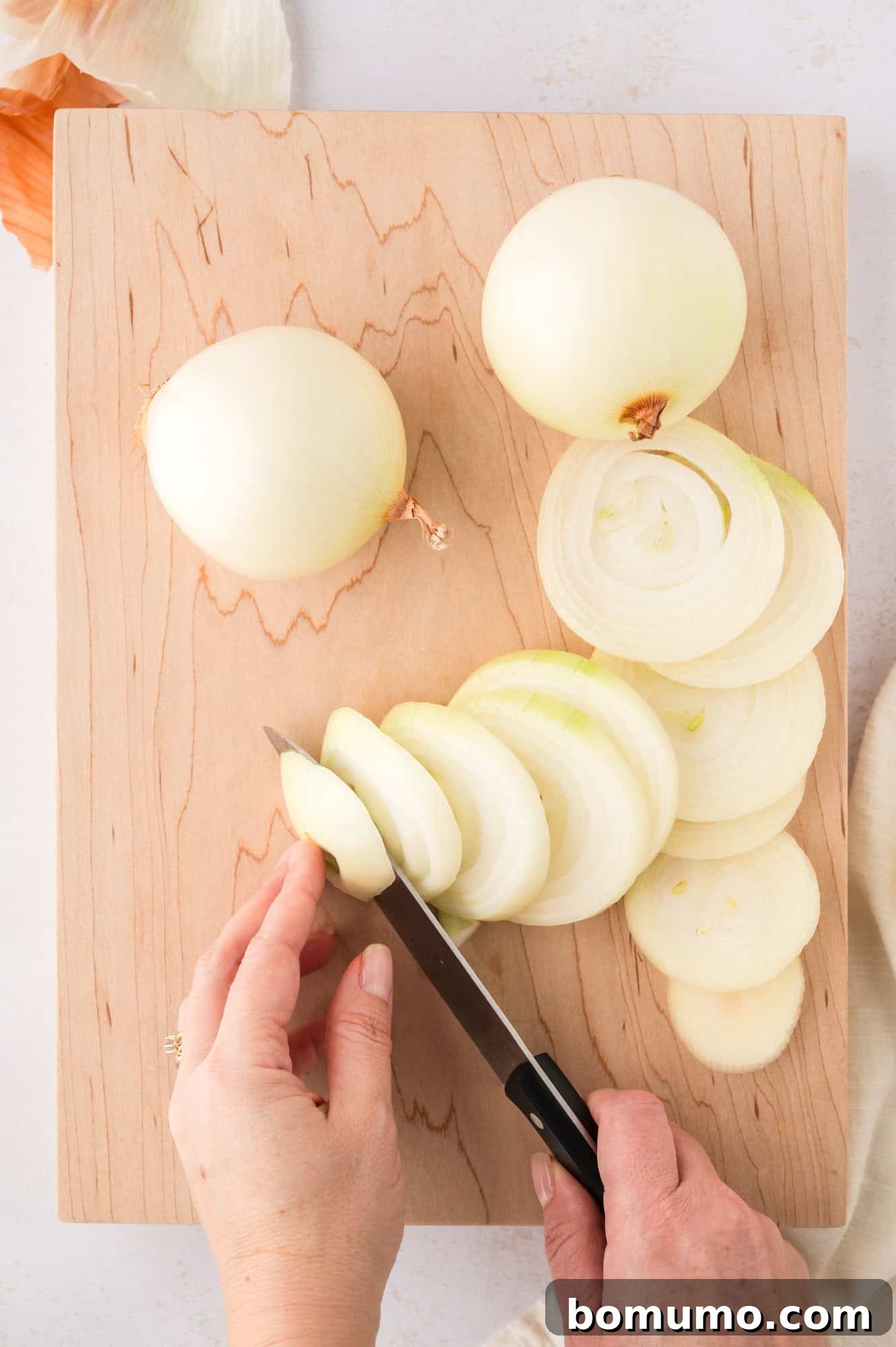 Neatly sliced onion pieces arranged on a cutting board, ready for the pan, demonstrating proper preparation for sautéed onions.