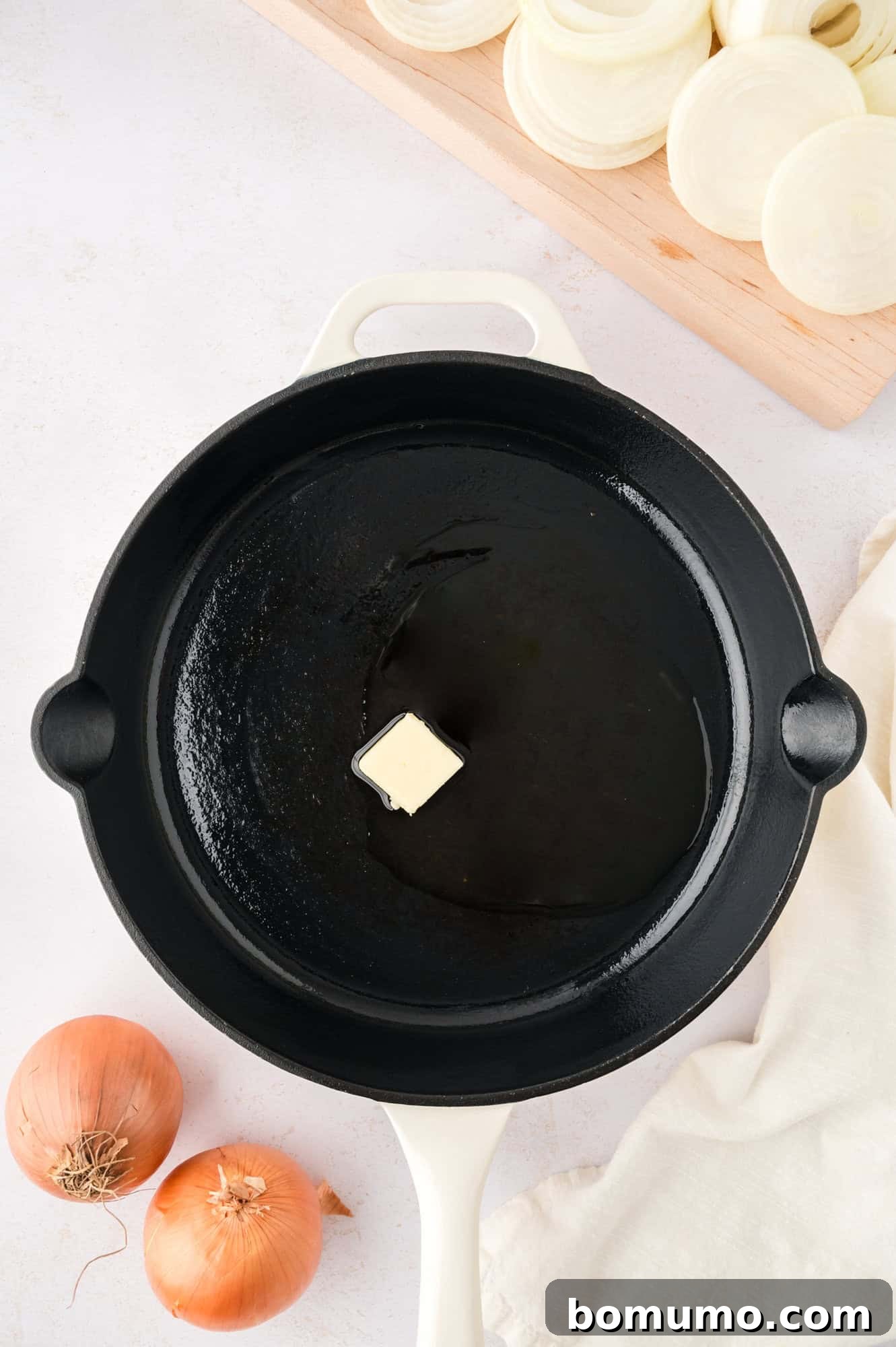A mixture of butter and olive oil shimmering in a large black skillet, indicating it's perfectly heated for cooking sautéed onions.