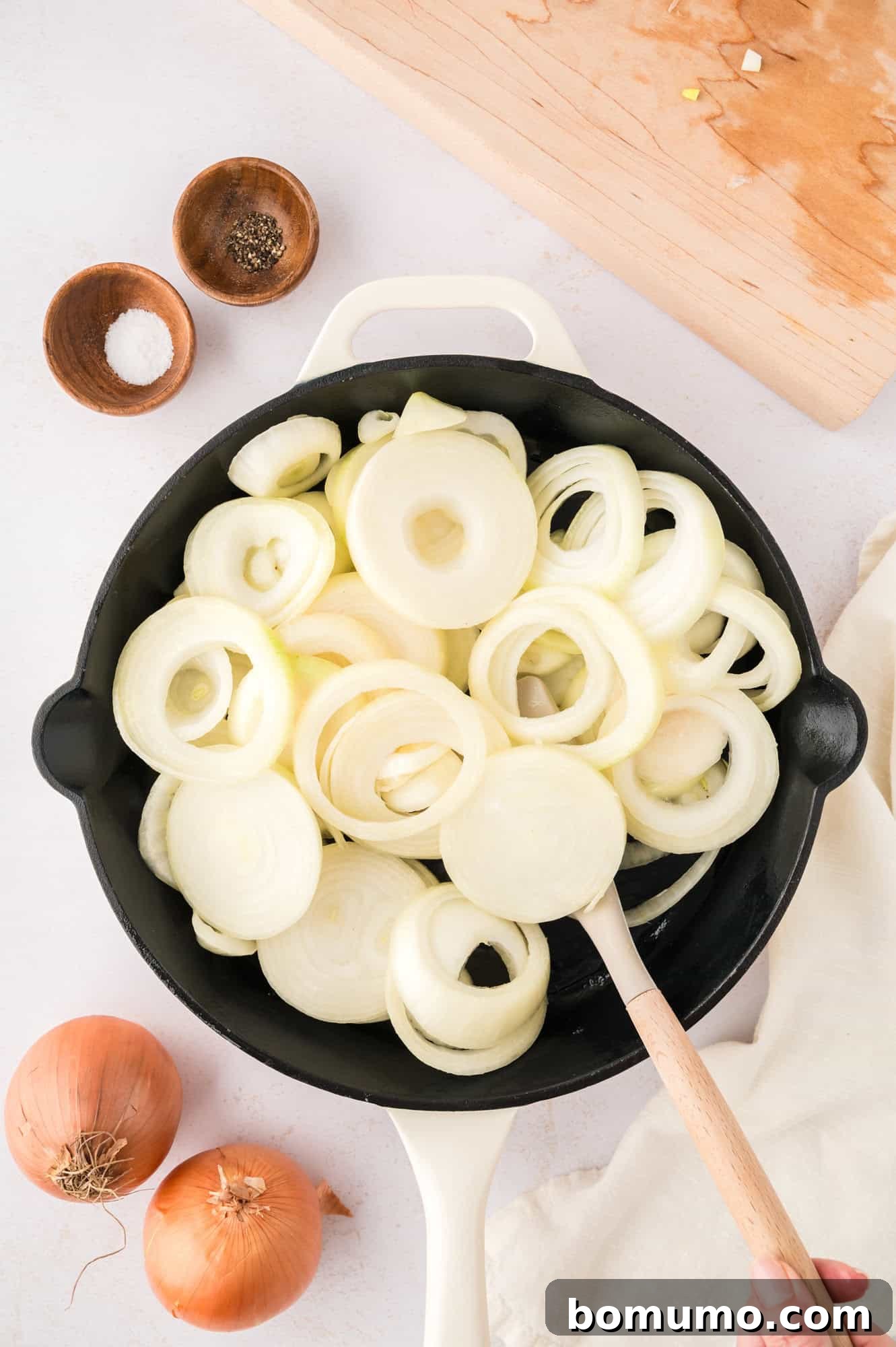 Freshly sliced raw onion rounds spread out in a large black skillet, ready to begin the sautéing process.