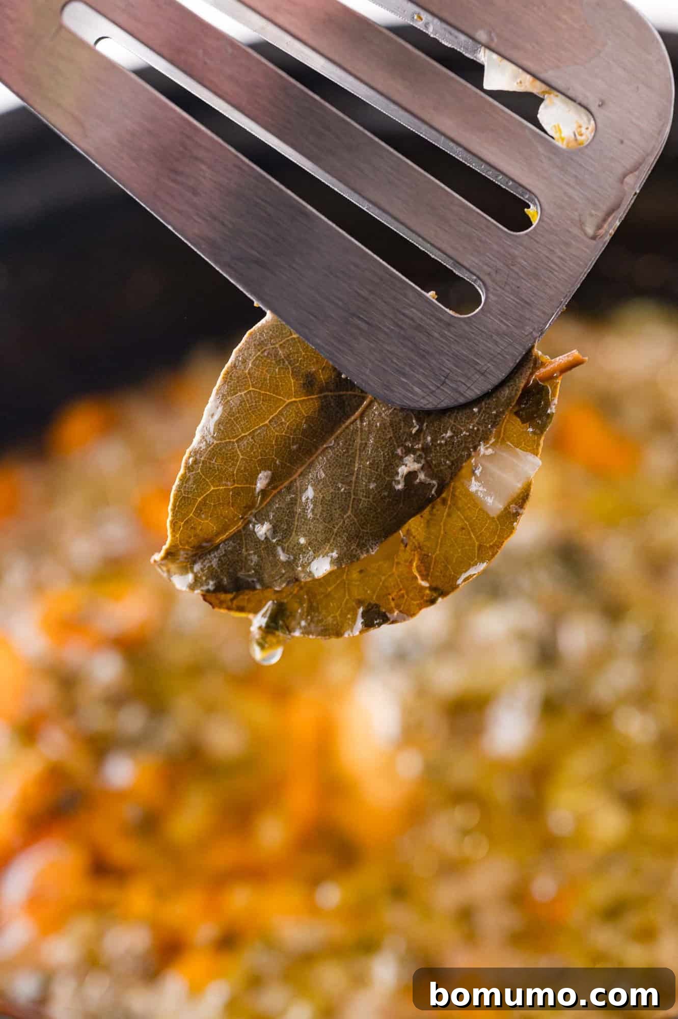 A bay leaf being carefully removed from the creamy chicken wild rice soup in the slow cooker.