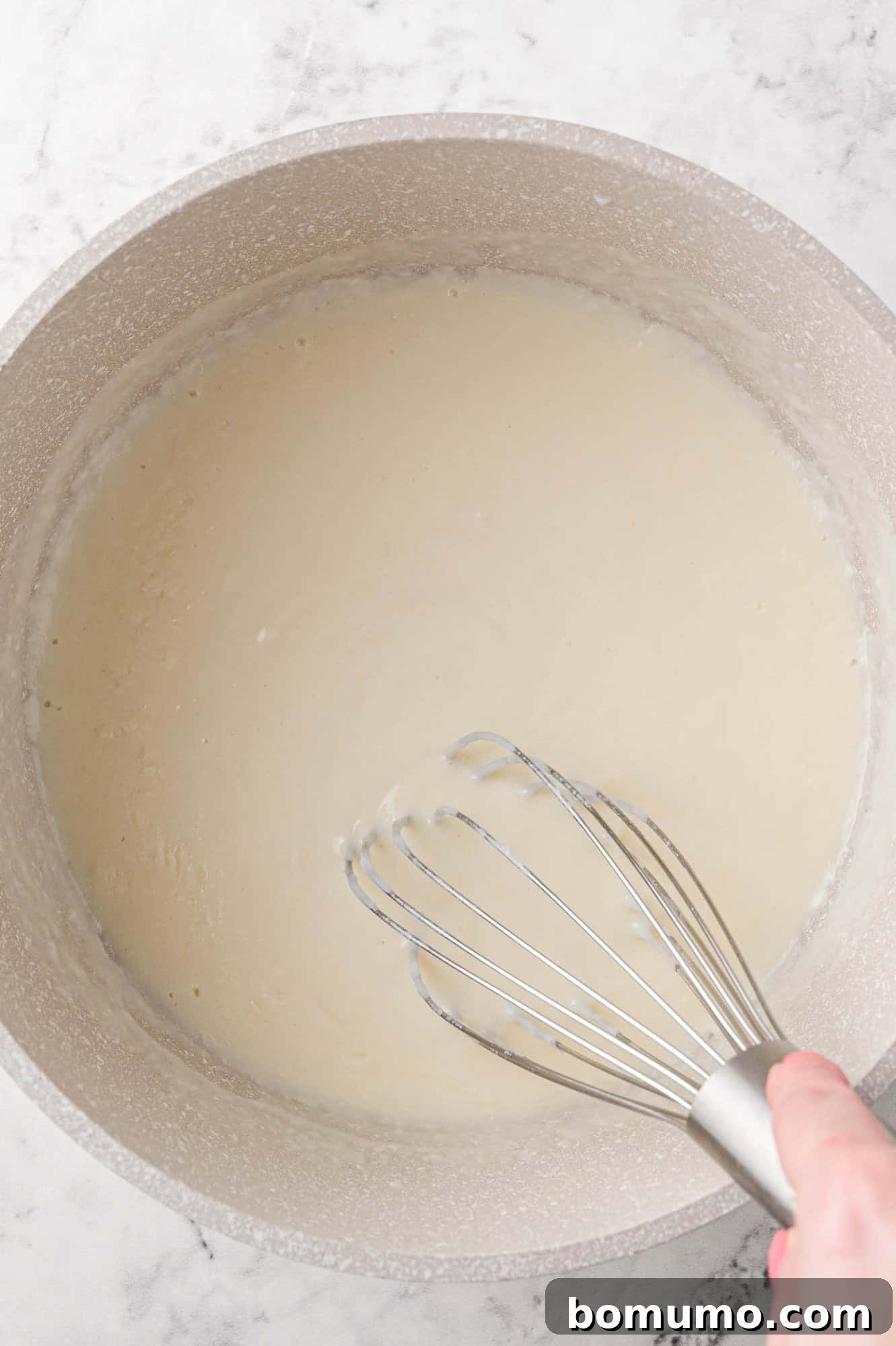 A white sauce being vigorously whisked in a saucepan on the stovetop.