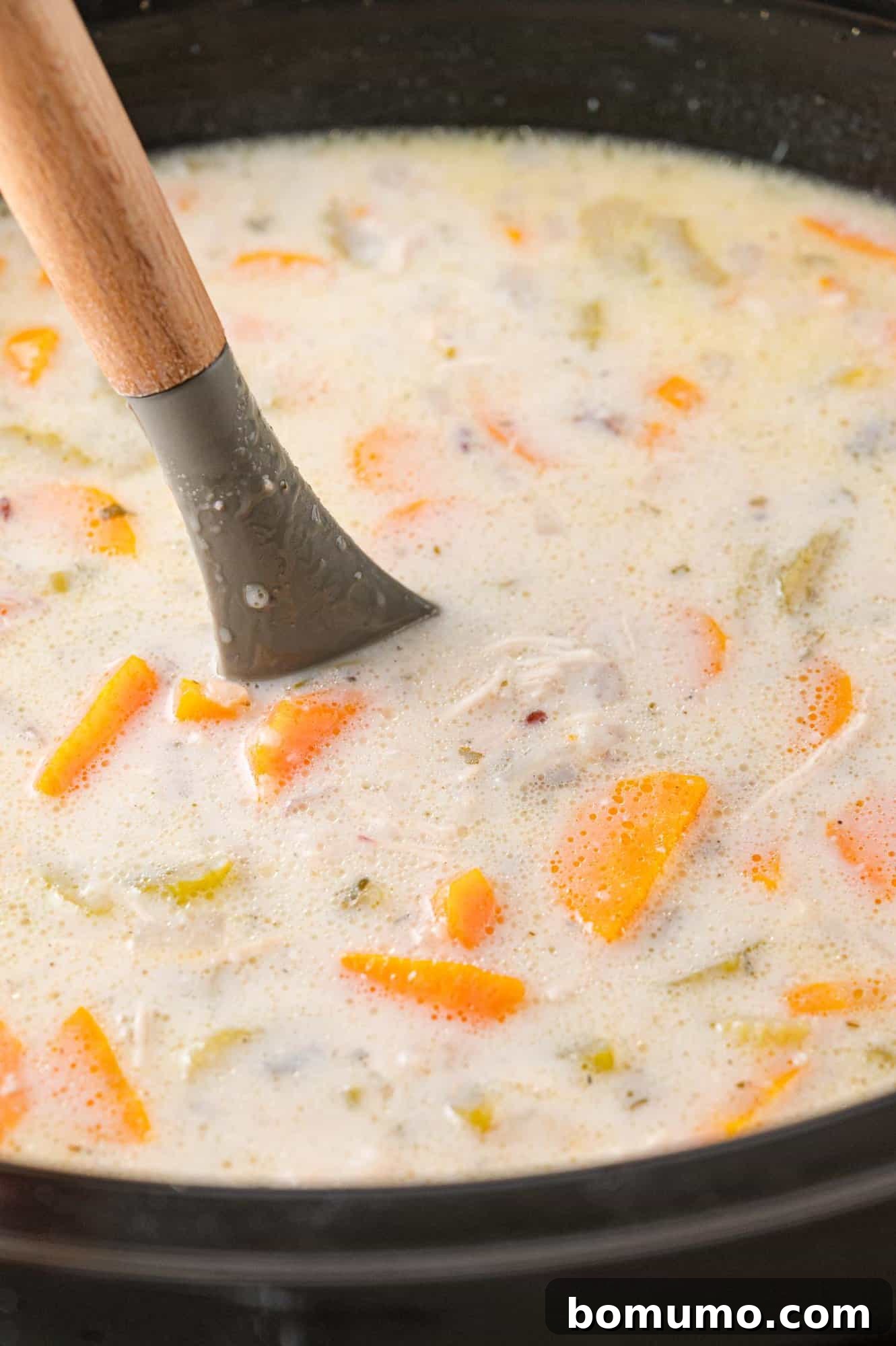 The finished white sauce being gently stirred into the crockpot chicken wild rice soup.