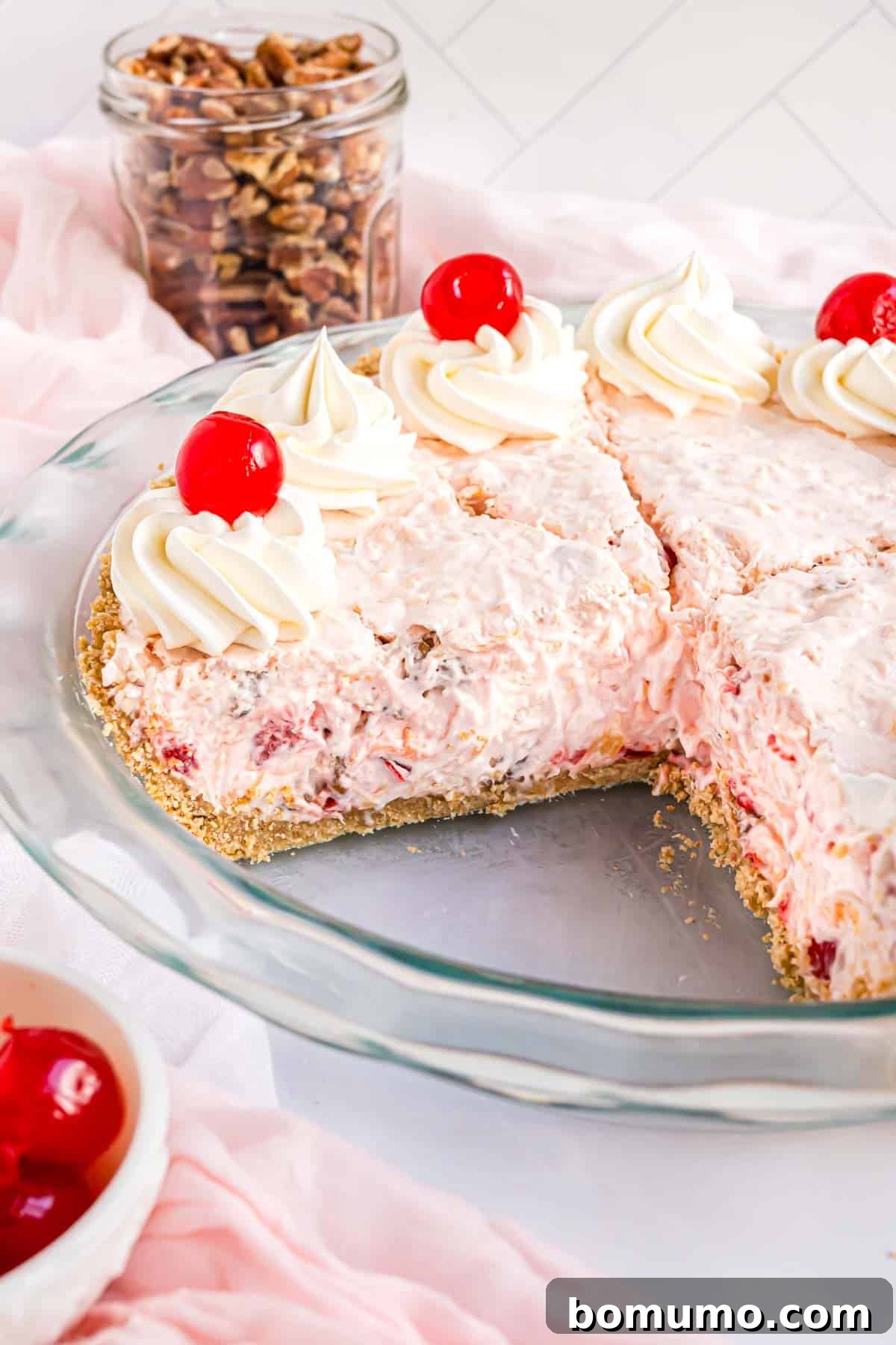 Golden Treasure Pie 2 A beautifully prepared Millionaire Pie, garnished with bright red maraschino cherries and a swirl of whipped cream. One slice has been carefully removed, revealing the creamy, textured filling within a golden graham cracker crust.