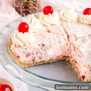 Millionaire pie topped with cherries and whipped cream, one slice removed from pie plate.