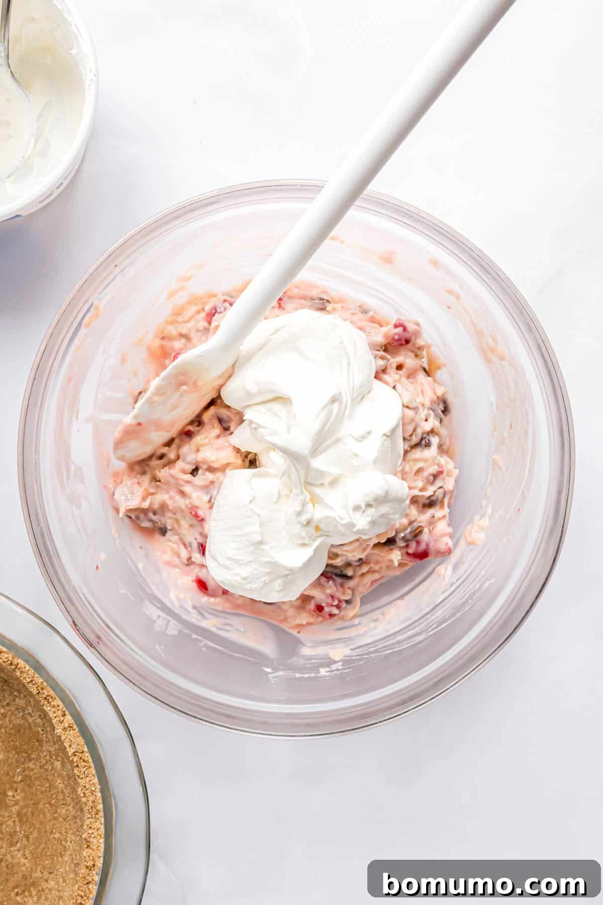 Golden Treasure Pie 7 A generous dollop of whipped cream (Cool Whip) freshly added to the fruit and nut filling mixture in a glass bowl, waiting to be gently folded in to create the Millionaire Pie's creamy texture.