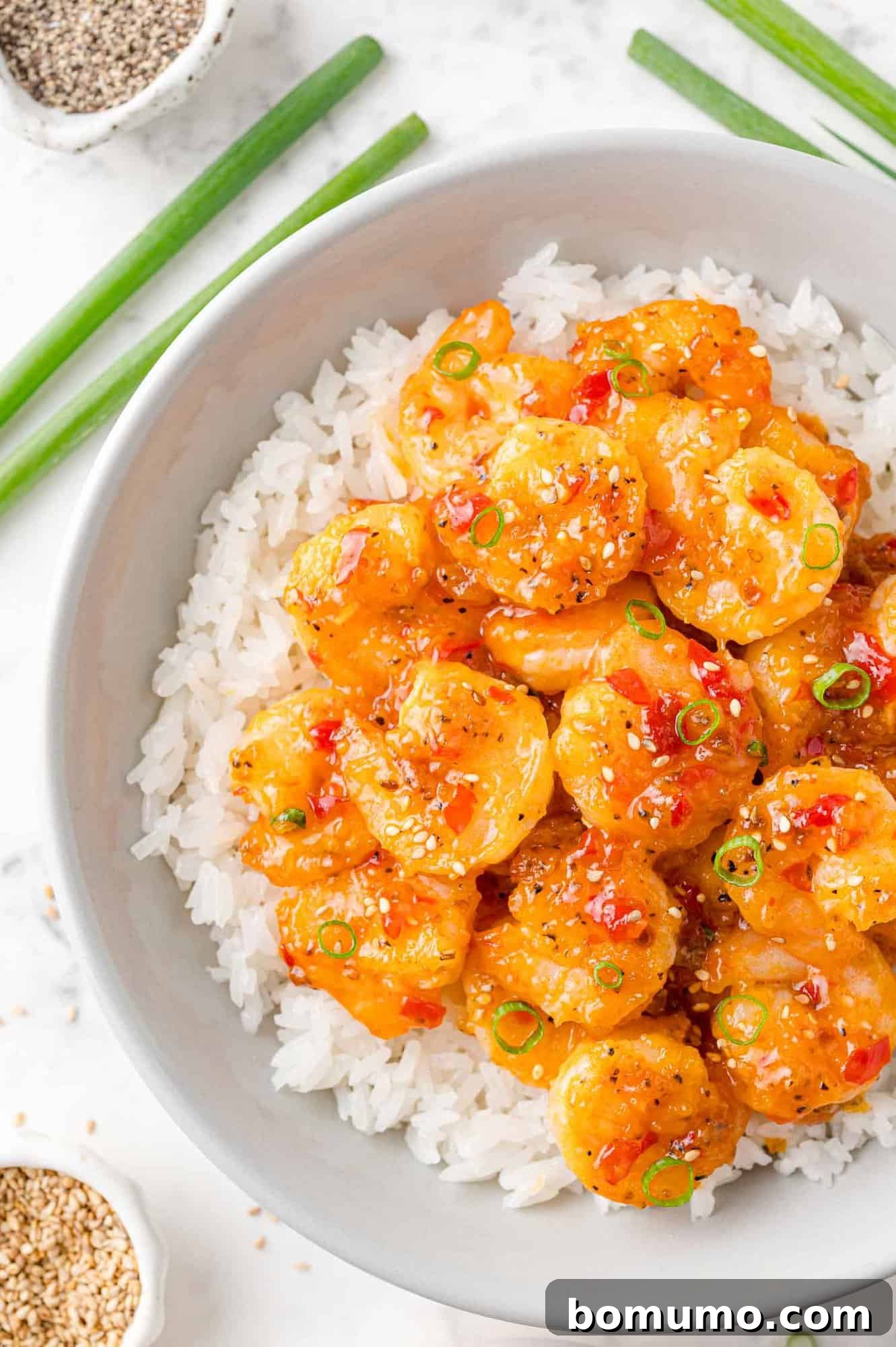 Firecracker shrimp served on a bed of fluffy white rice, garnished with vibrant green onions and a sprinkle of sesame seeds, ready to be enjoyed.