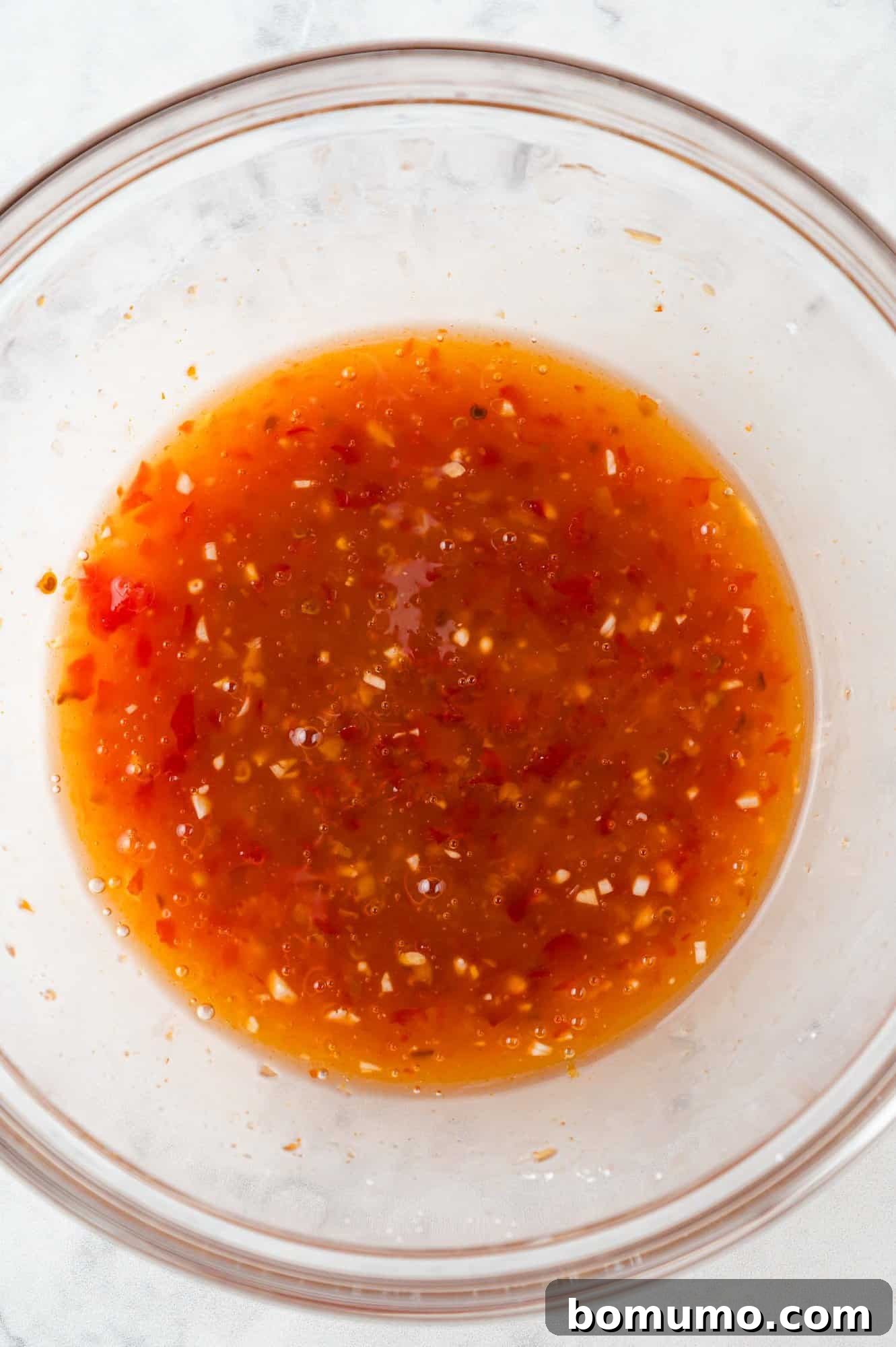 The vibrant orange-red Firecracker Shrimp sauce, perfectly mixed in a small glass bowl, showcasing its smooth and inviting consistency.