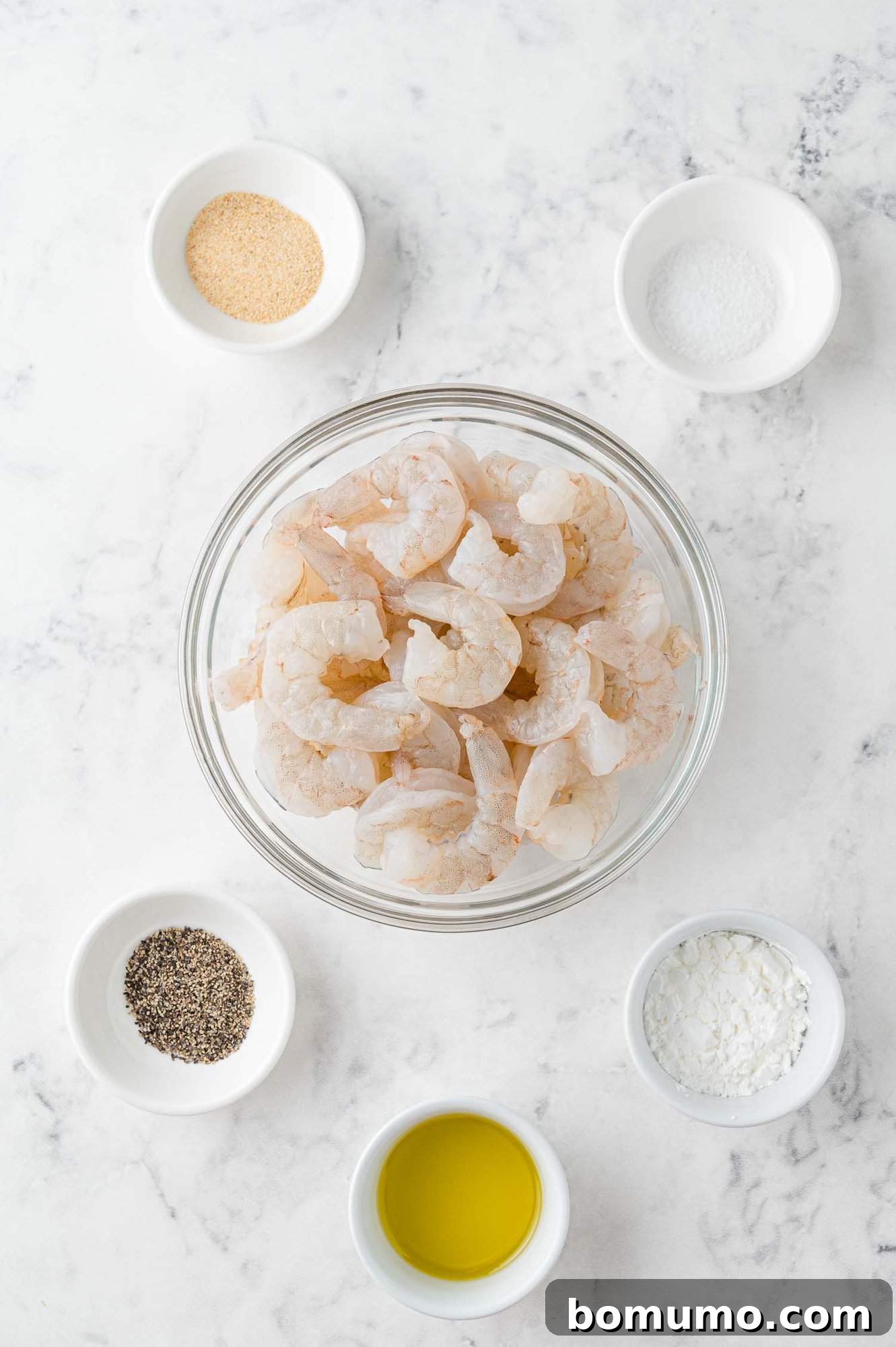 Raw shrimp ready for seasoning, alongside bowls of cornstarch, garlic powder, salt, and pepper, showcasing the prep stage for Firecracker Shrimp.