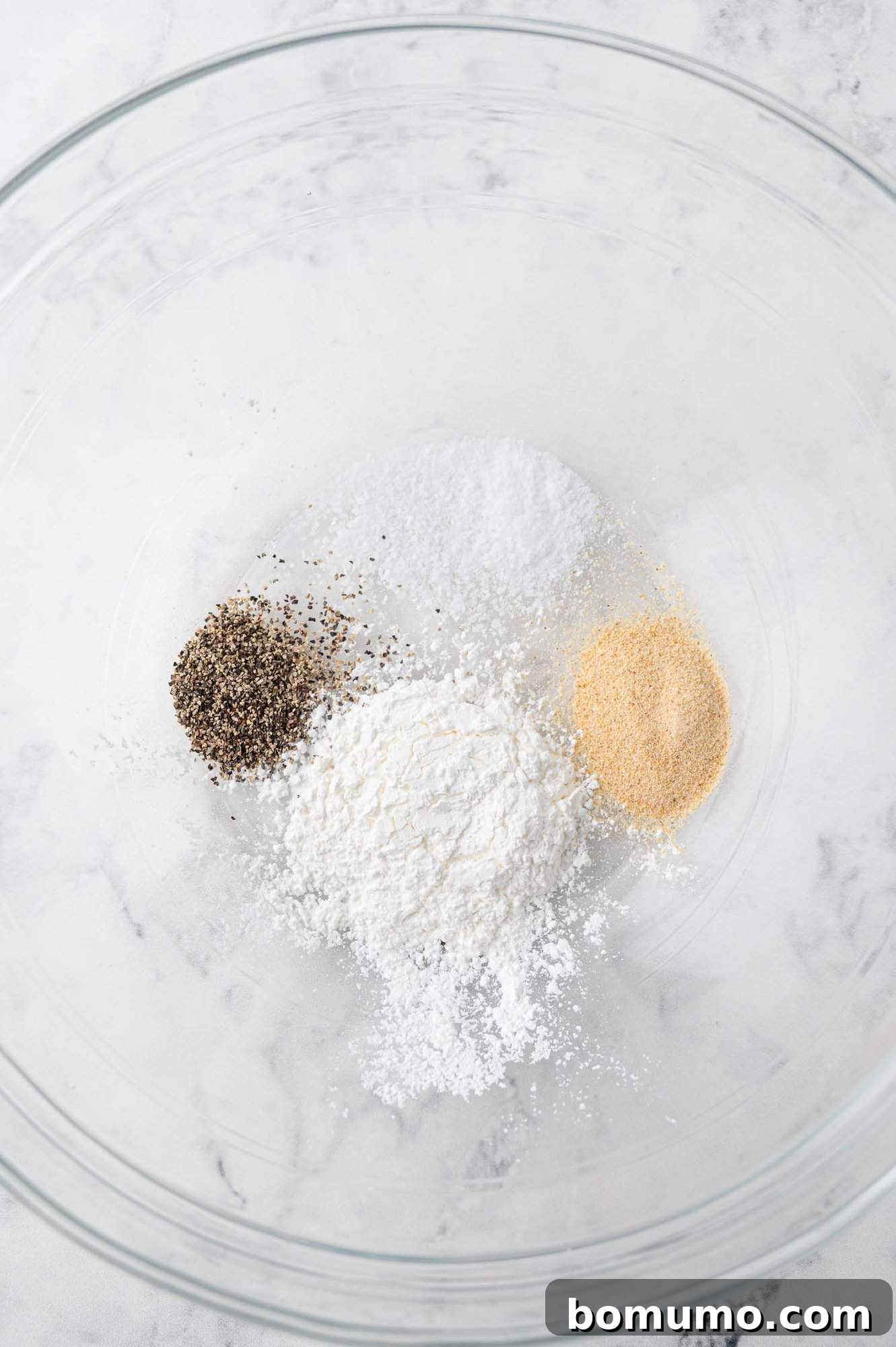 A glass mixing bowl holds a blend of cornstarch and seasonings, creating the perfect coating mixture for Firecracker Shrimp.