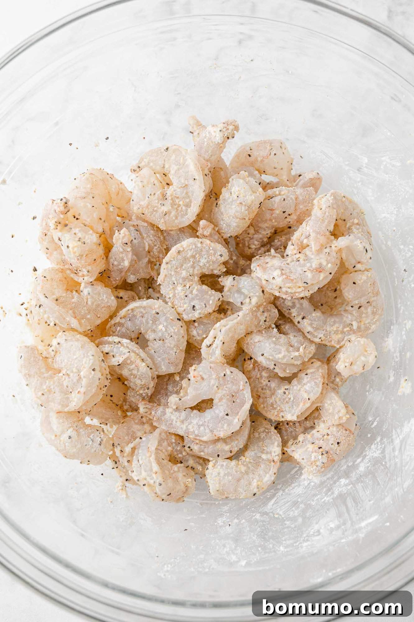 Plump shrimp evenly coated with cornstarch and seasonings, glistening and ready to be cooked for a delicious Firecracker Shrimp dish.