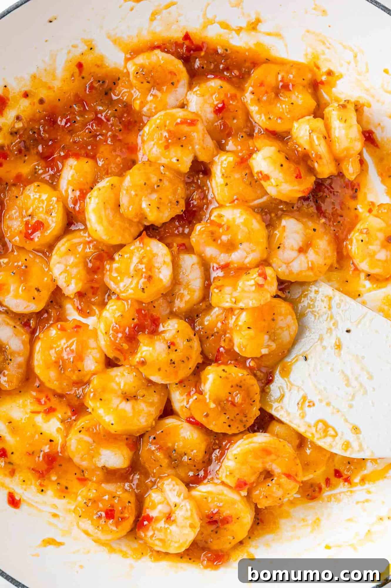 The vibrant red-orange Firecracker sauce being poured over the cooked shrimp in a skillet, ready to be tossed and simmered.