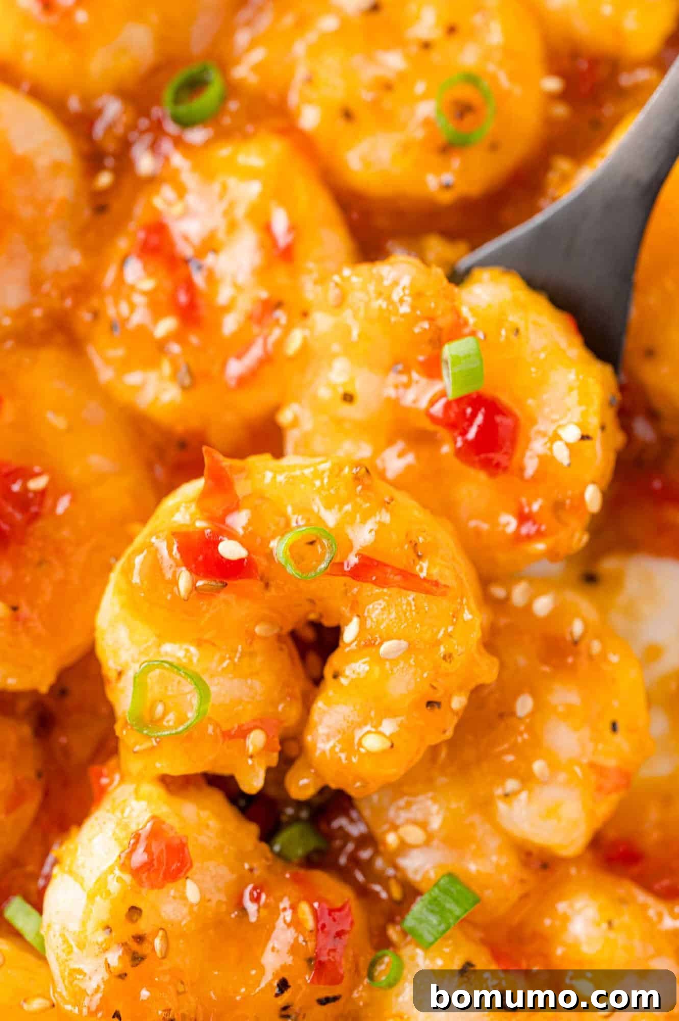 A black serving spoon scooping glistening, sauced Firecracker Shrimp from a pan, ready to be served.