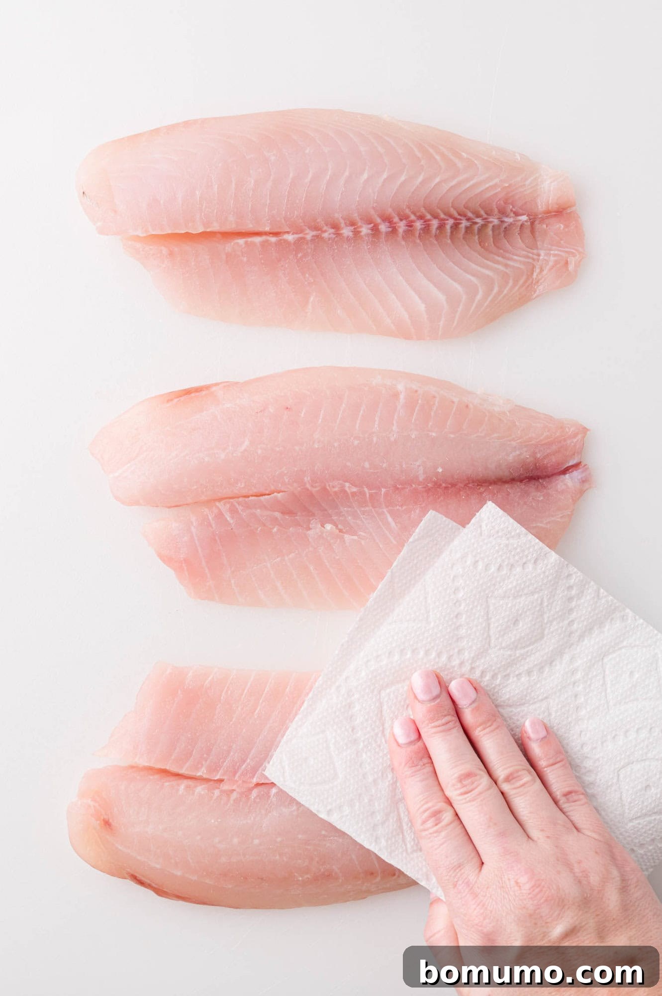 A tilapia fillet being carefully patted dry with a paper towel, a crucial step for achieving optimal texture during air frying.