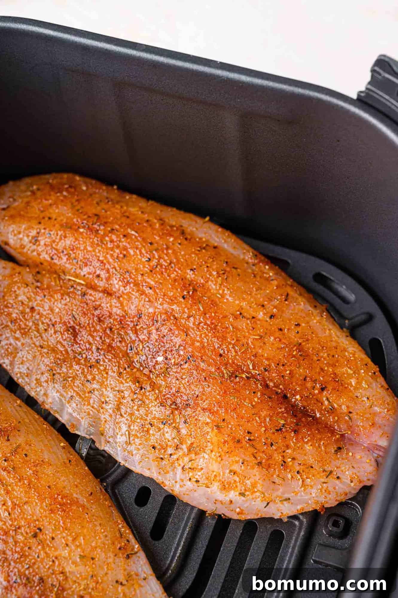 Uncooked, seasoned tilapia fillets neatly arranged in a single layer within the air fryer basket, perfectly spaced for even cooking.