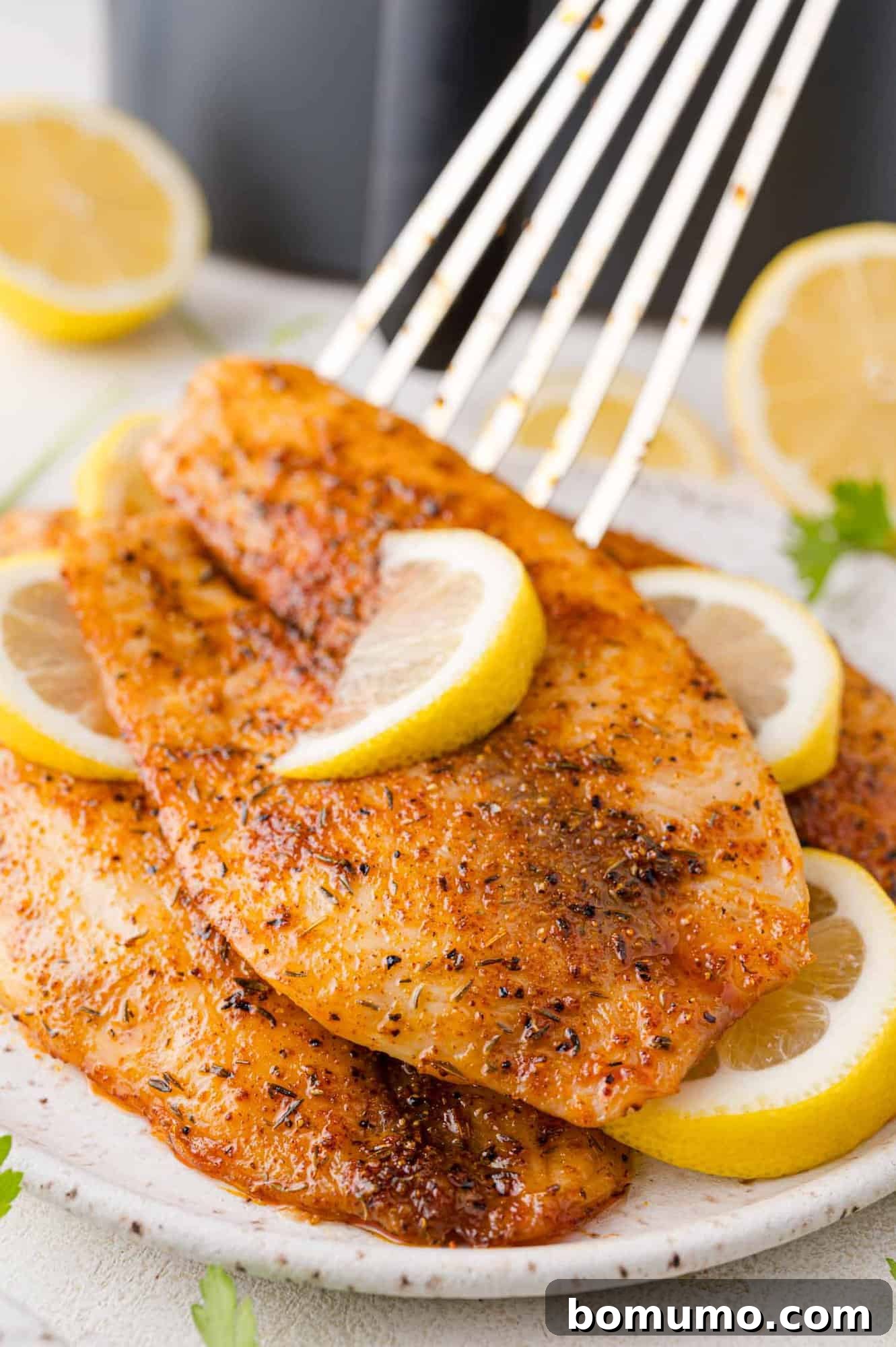 A perfectly cooked air fryer tilapia fillet, partially lifted by a fish spatula, adorned with a fresh lemon slice, ready to be enjoyed.