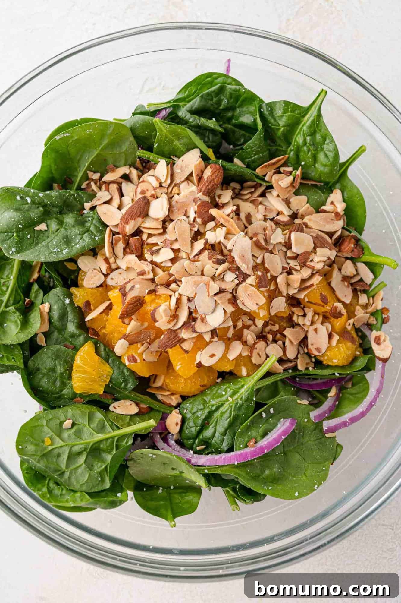 Toasted almonds and juicy mandarin oranges being carefully added to the freshly tossed salad base, enhancing its color and texture.