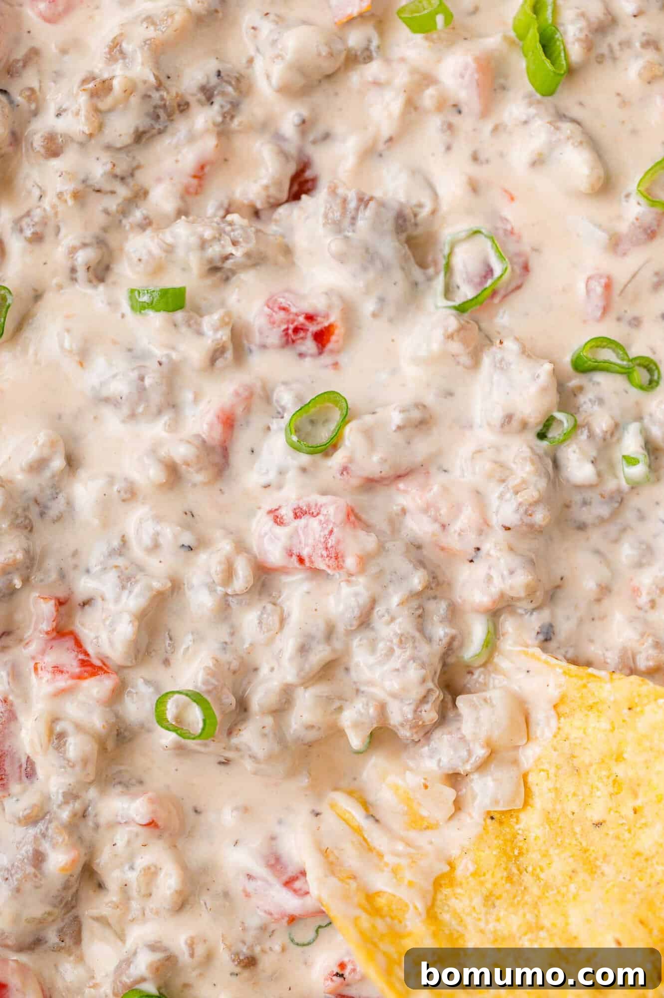 Sausage Cheese Bliss 8 Dip made from sausage, tomatoes, and cream cheese, being scooped with a yellow corn tortilla chip.