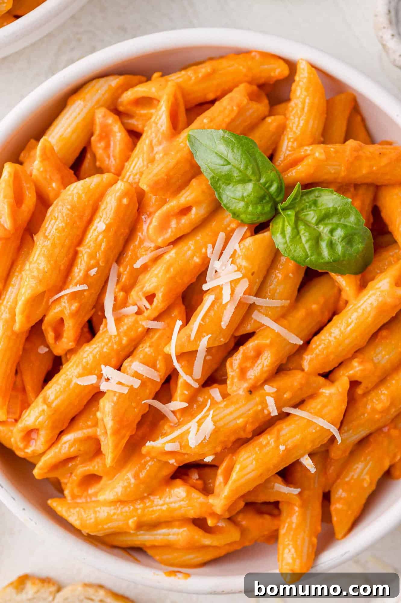Vodka pasta in a white bowl, garnished with parmesan cheese and basil.