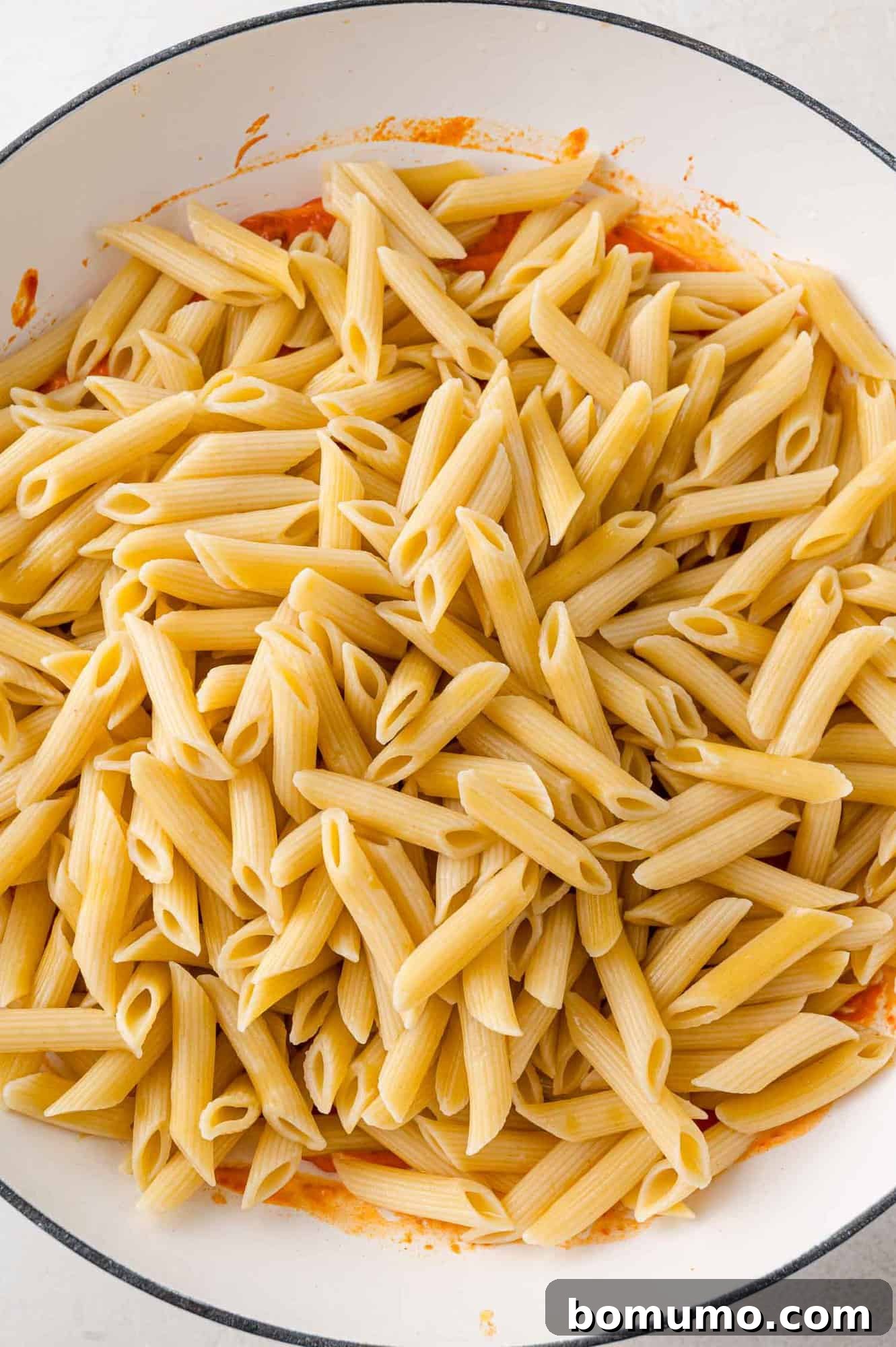 Cooked penne pasta added to sauce.