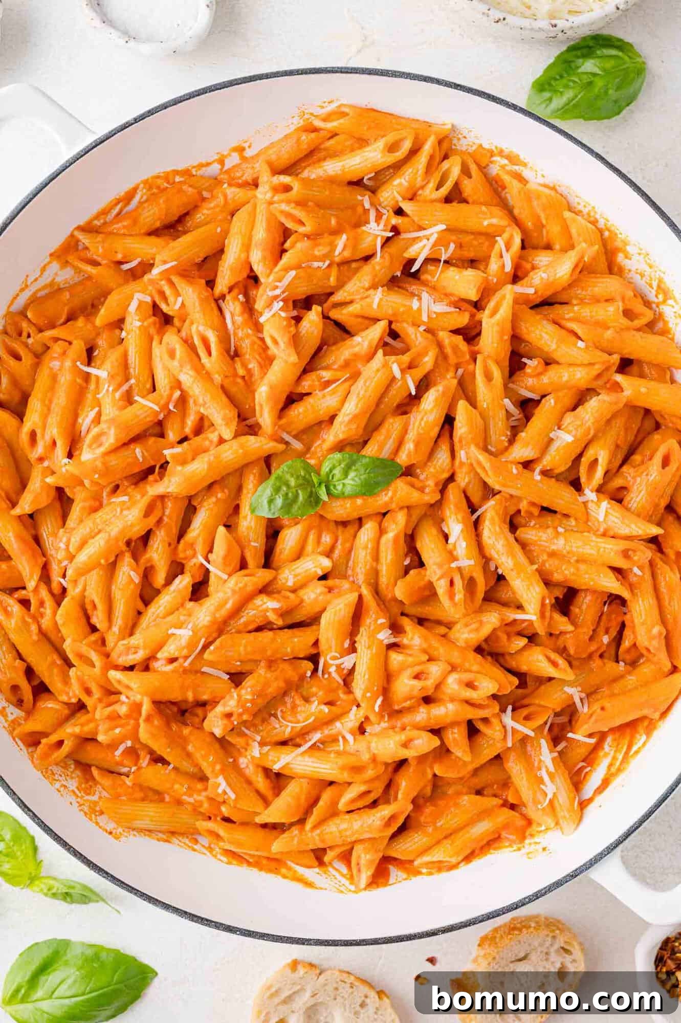 Large white bowl filled with penne pasta and vodka sauce, topped with basil and cheese.