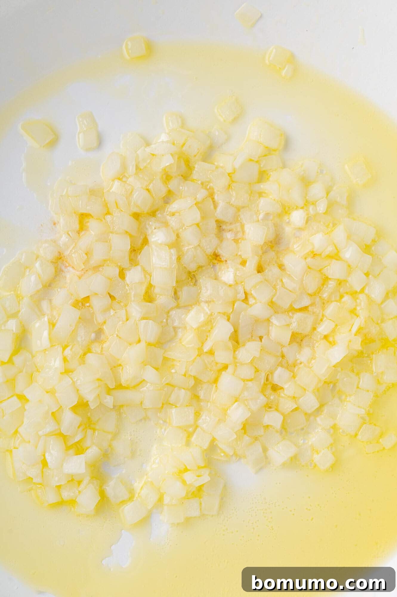 Onions and garlic sautéed in a white frying pan.