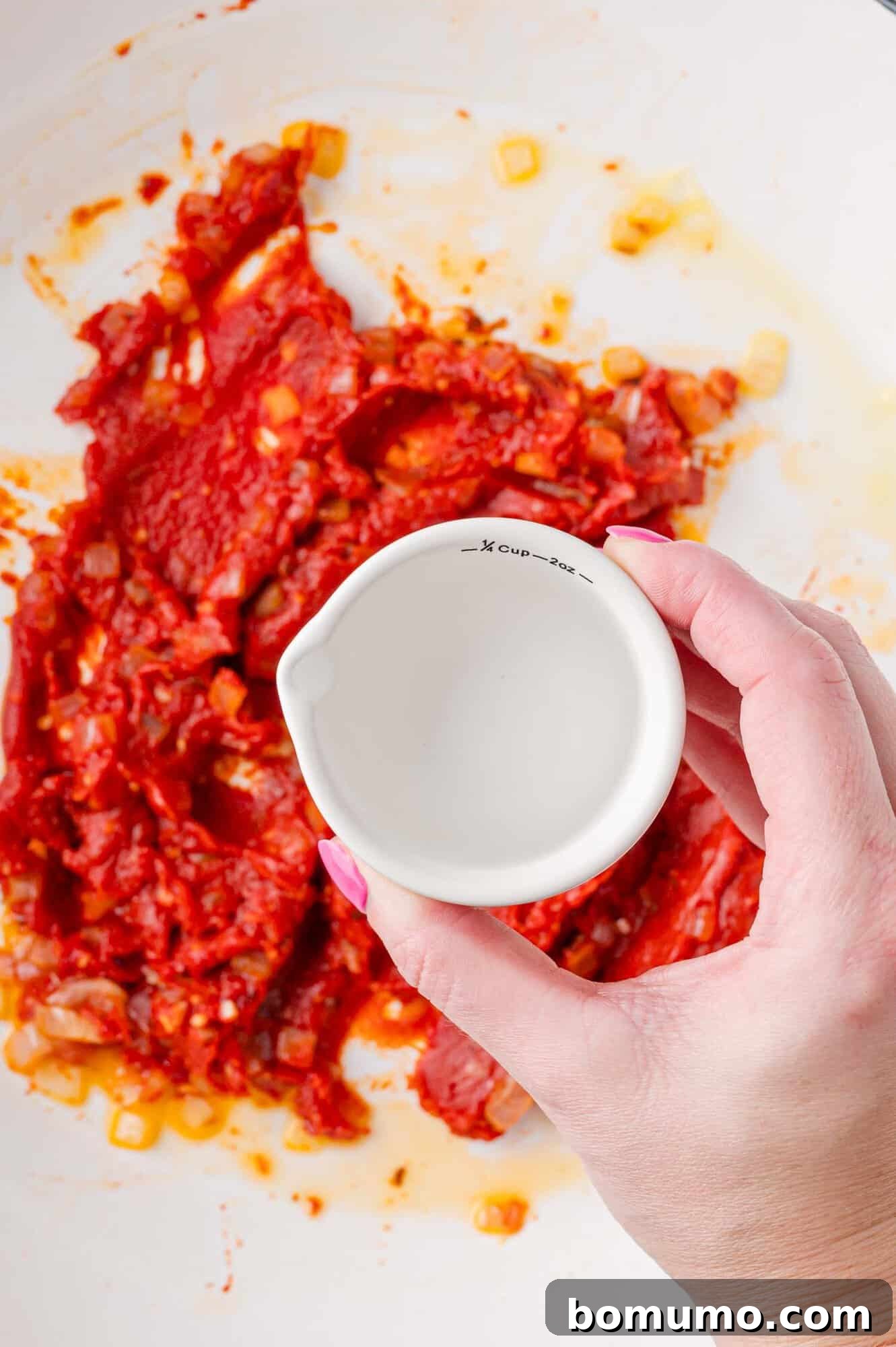 Vodka being added to sautéed onions, garlic, and tomato paste.