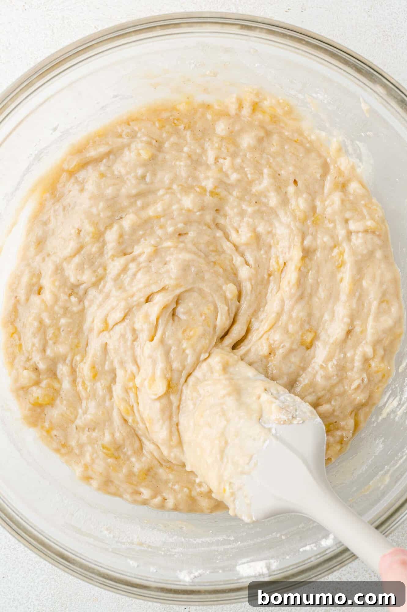 Smooth, combined banana bread batter in a clear glass bowl, before the chocolate chips are added.