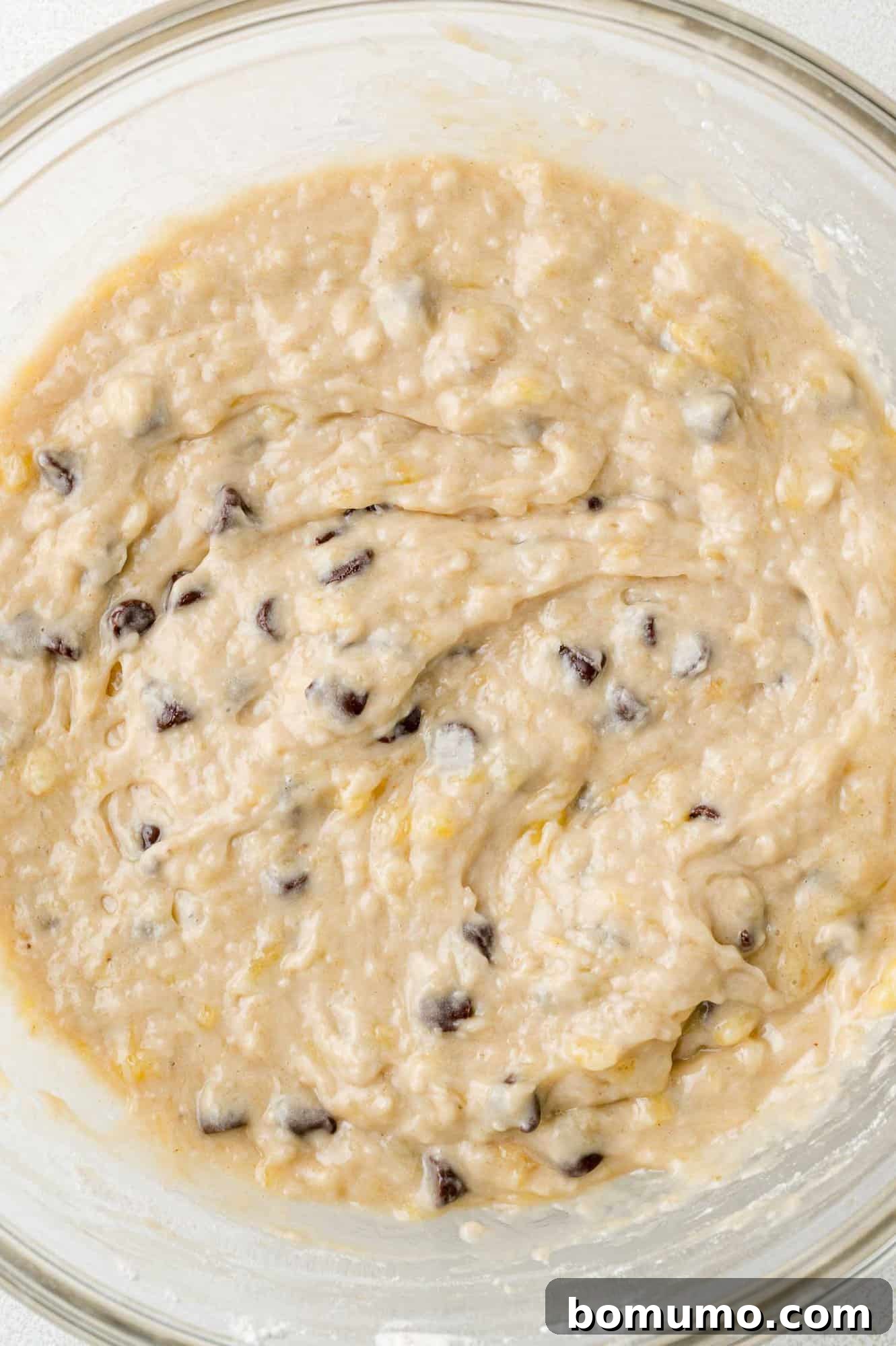 Banana bread batter with chocolate chips folded in, resting in a clear glass mixing bowl.