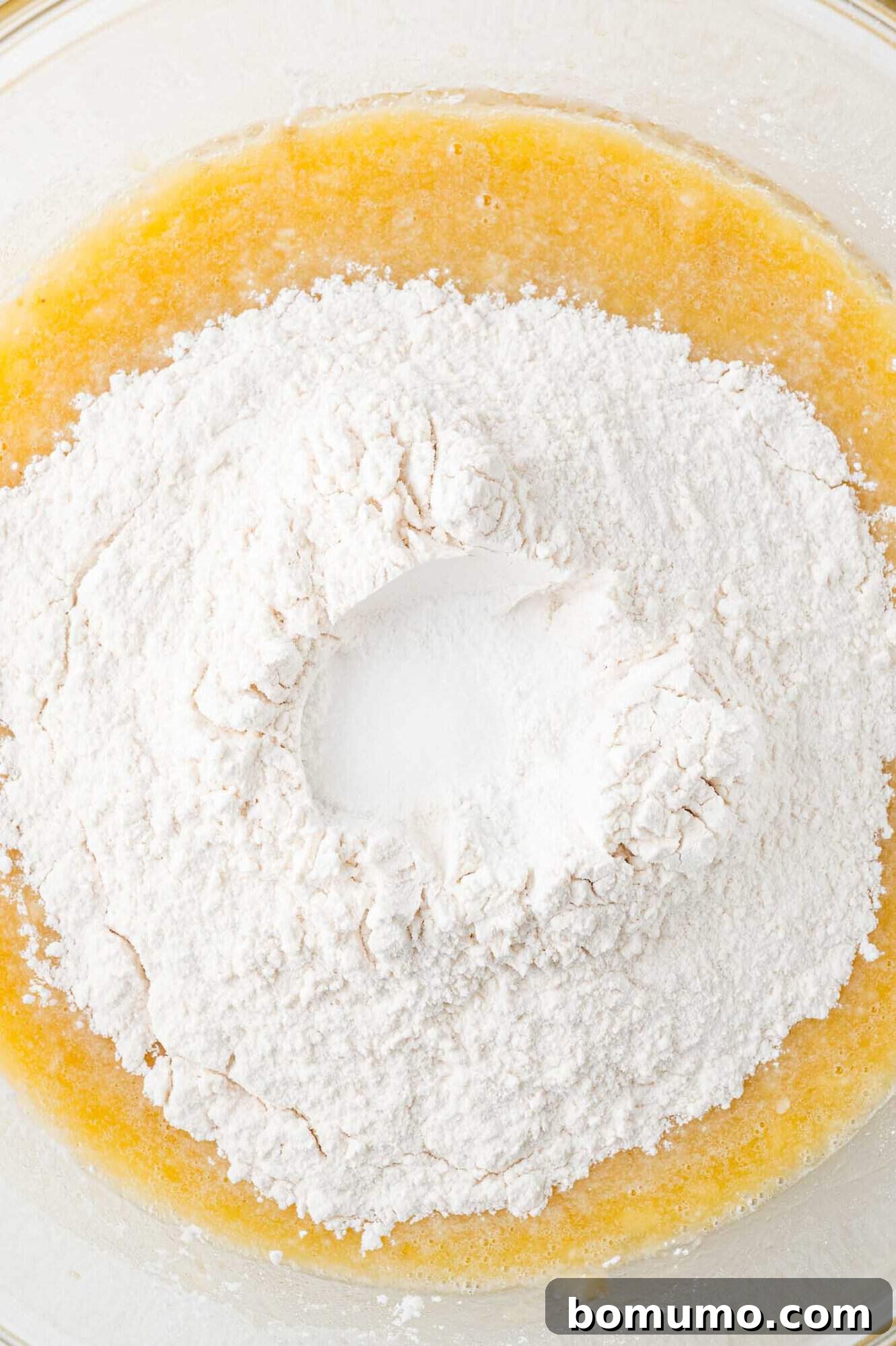 Dry ingredients (flour, baking soda, baking powder, salt) layered on top of the wet banana mixture, prior to being combined.