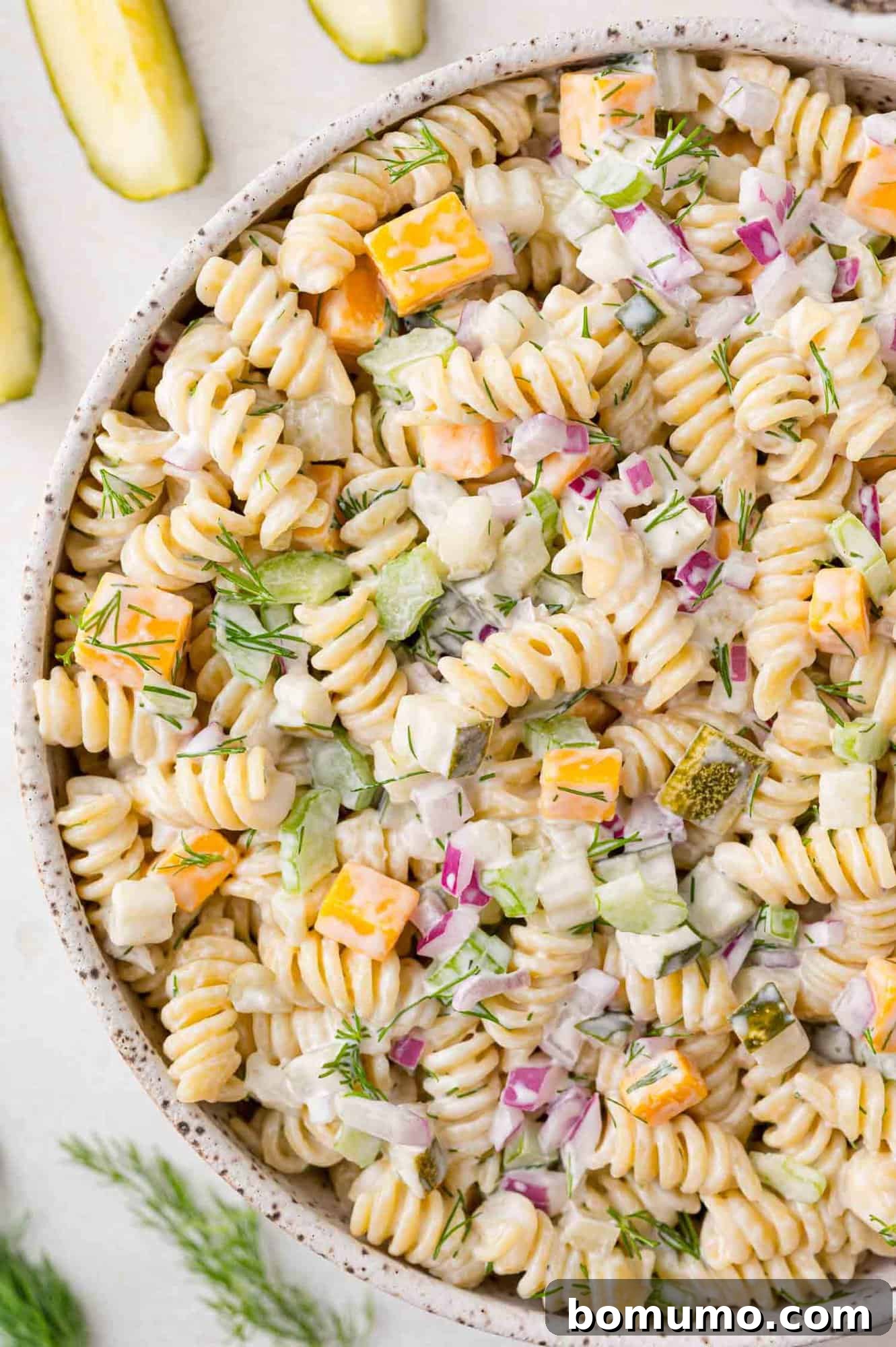 Dill pickle pasta salad in a large bowl, garnished with fresh dill and surrounded by pickles.