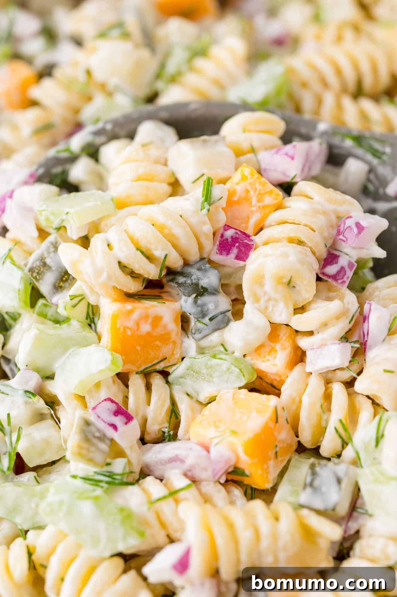 A scoop of dill pickle pasta salad served on a large spoon, ready to eat.