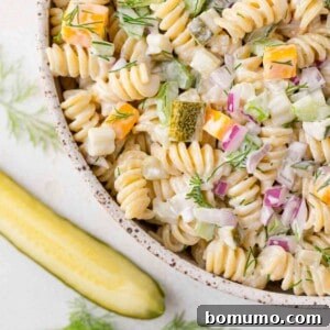 Dill pickle pasta salad with rotini pasta, in a bowl, with a dill pickle next to it.