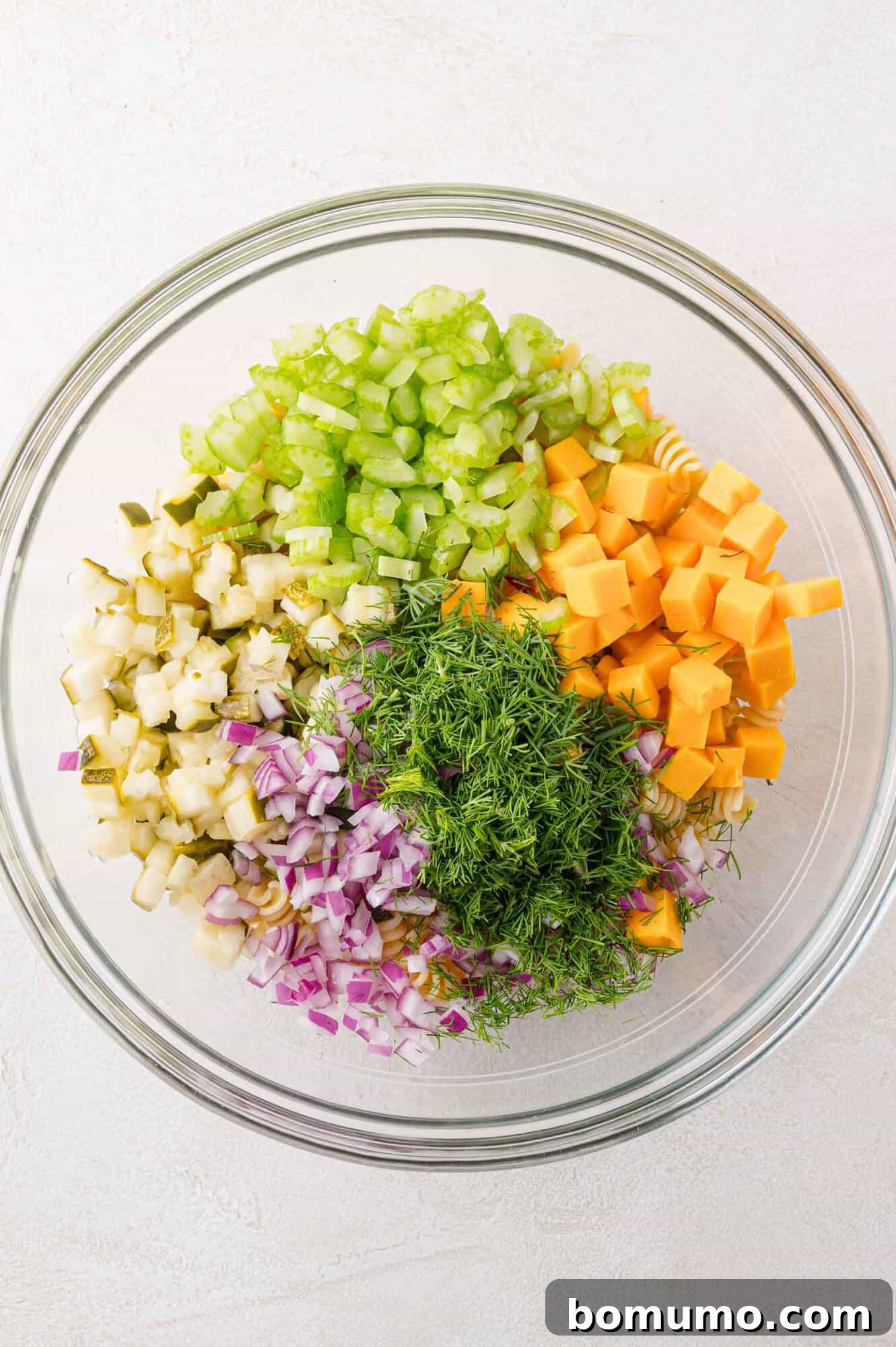 Various salad ingredients like pickles, cheese, and onion in a bowl, awaiting mixing.