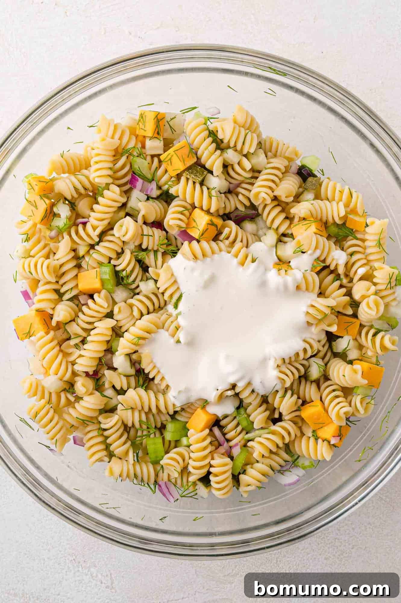 Creamy dressing poured over pasta salad, before mixing.