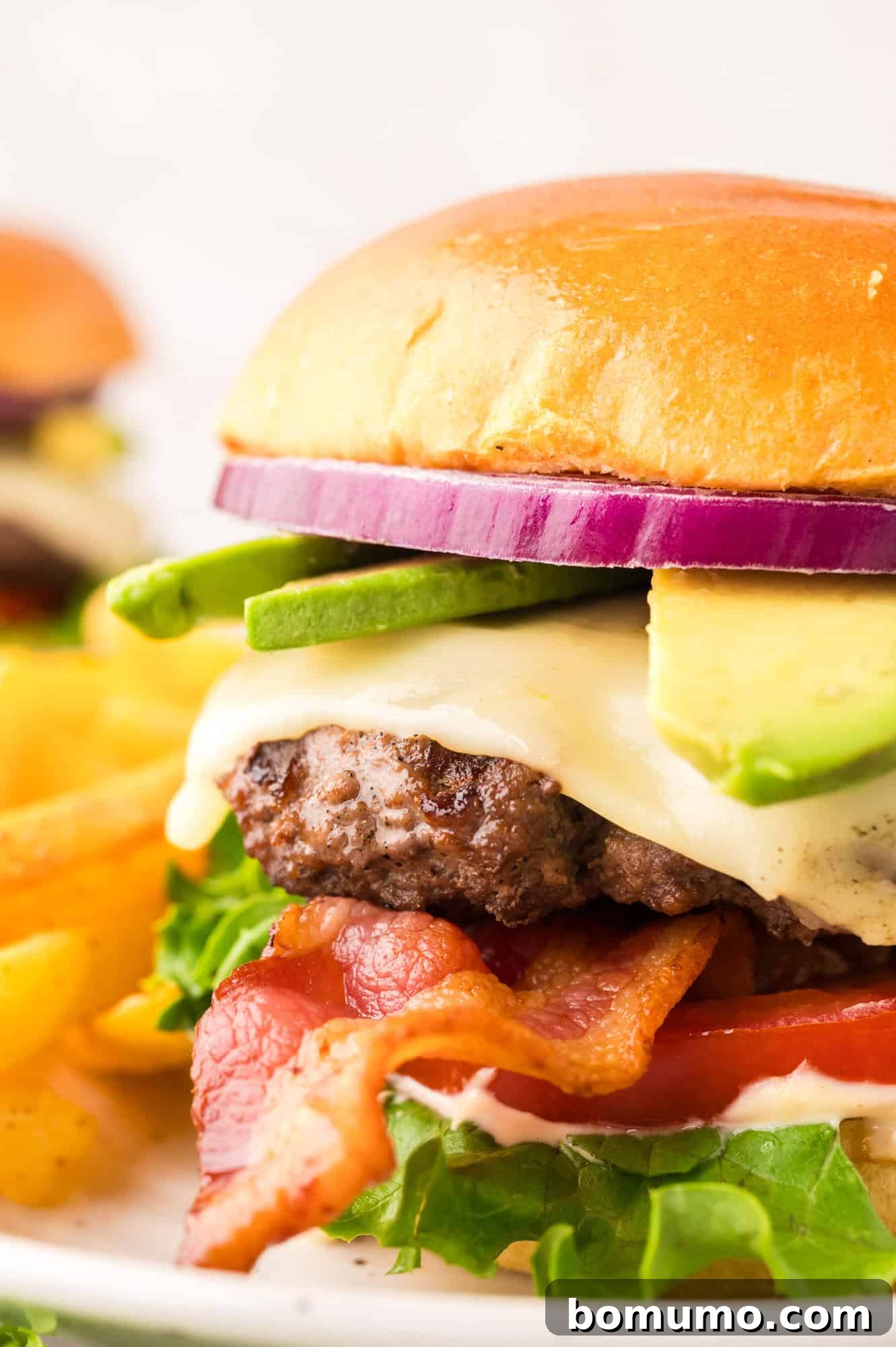 The Cali Dream Burger 2 A vibrant California burger showcasing layers of creamy avocado, crispy bacon, fresh lettuce, juicy tomato, and a perfectly cooked patty on a toasted bun.